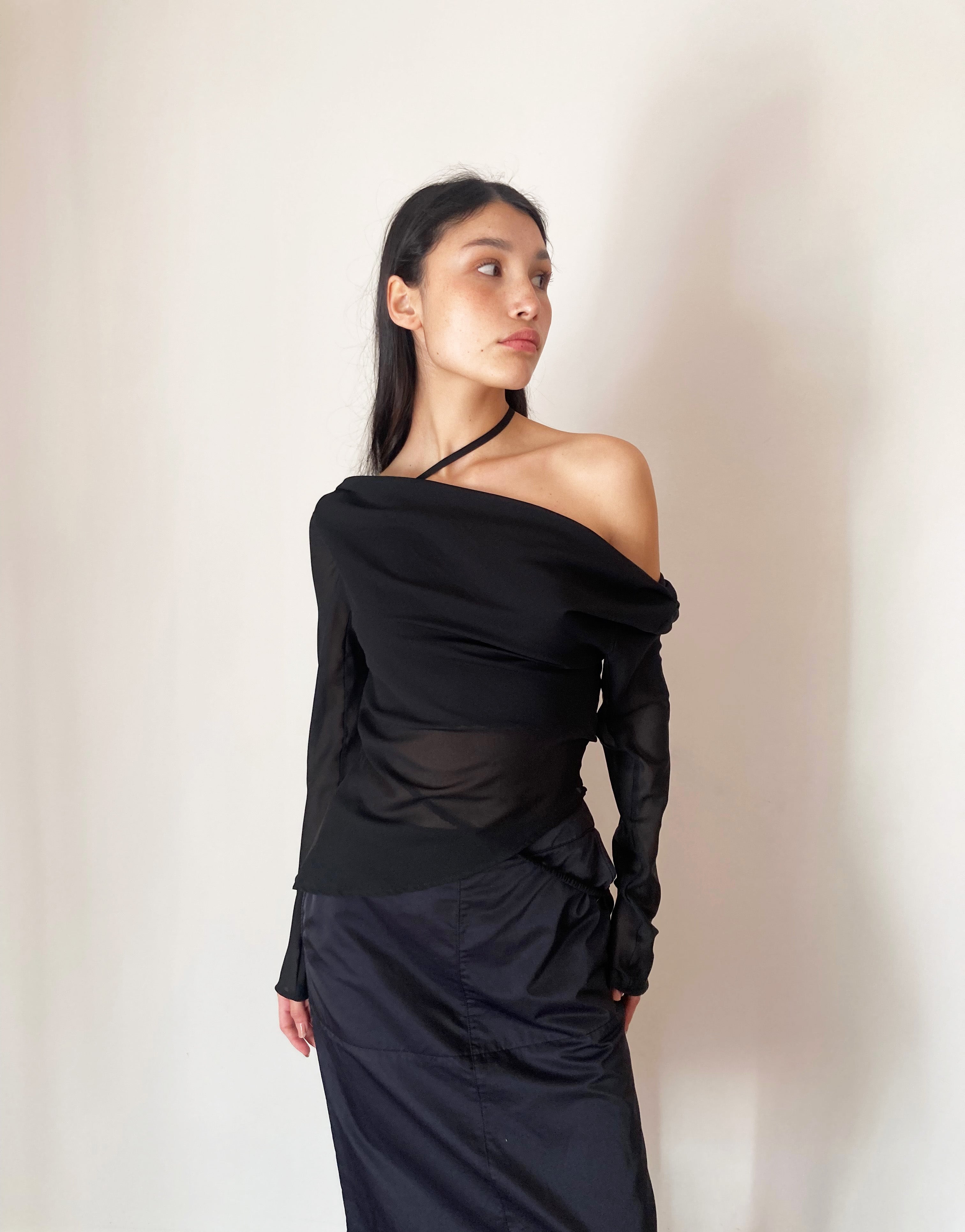 Woman wearing a black off-shoulder top and dark pants against a plain background. Made from 100% recycled material.