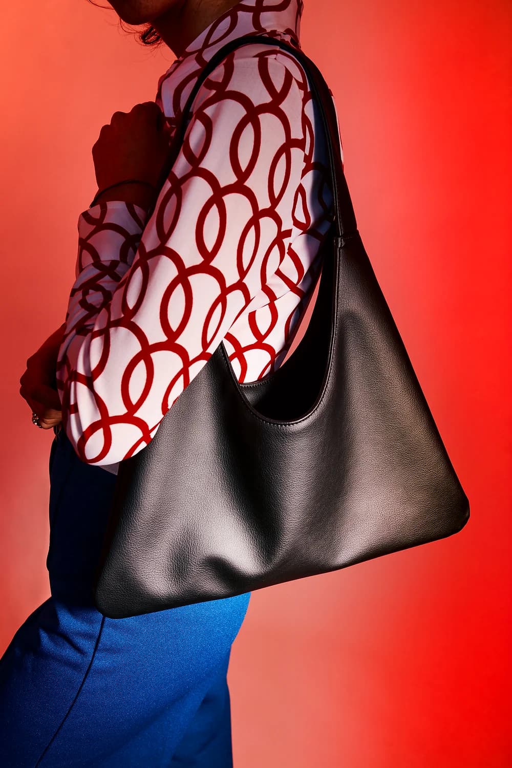 Person holding a black sustainable cactus leather handbag against a red background