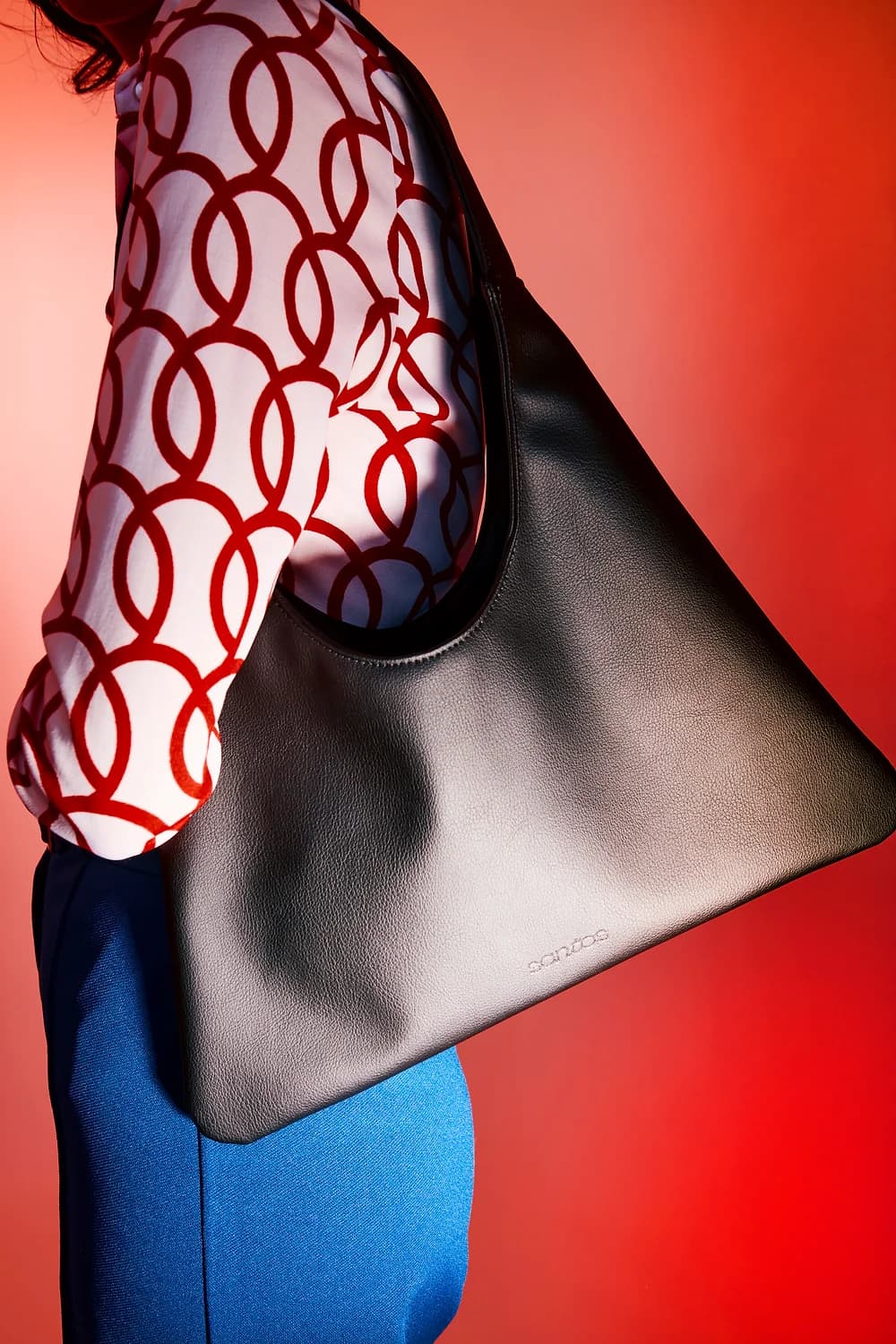 Person holding a black sustainable tote bag made from cactus leather against a red background