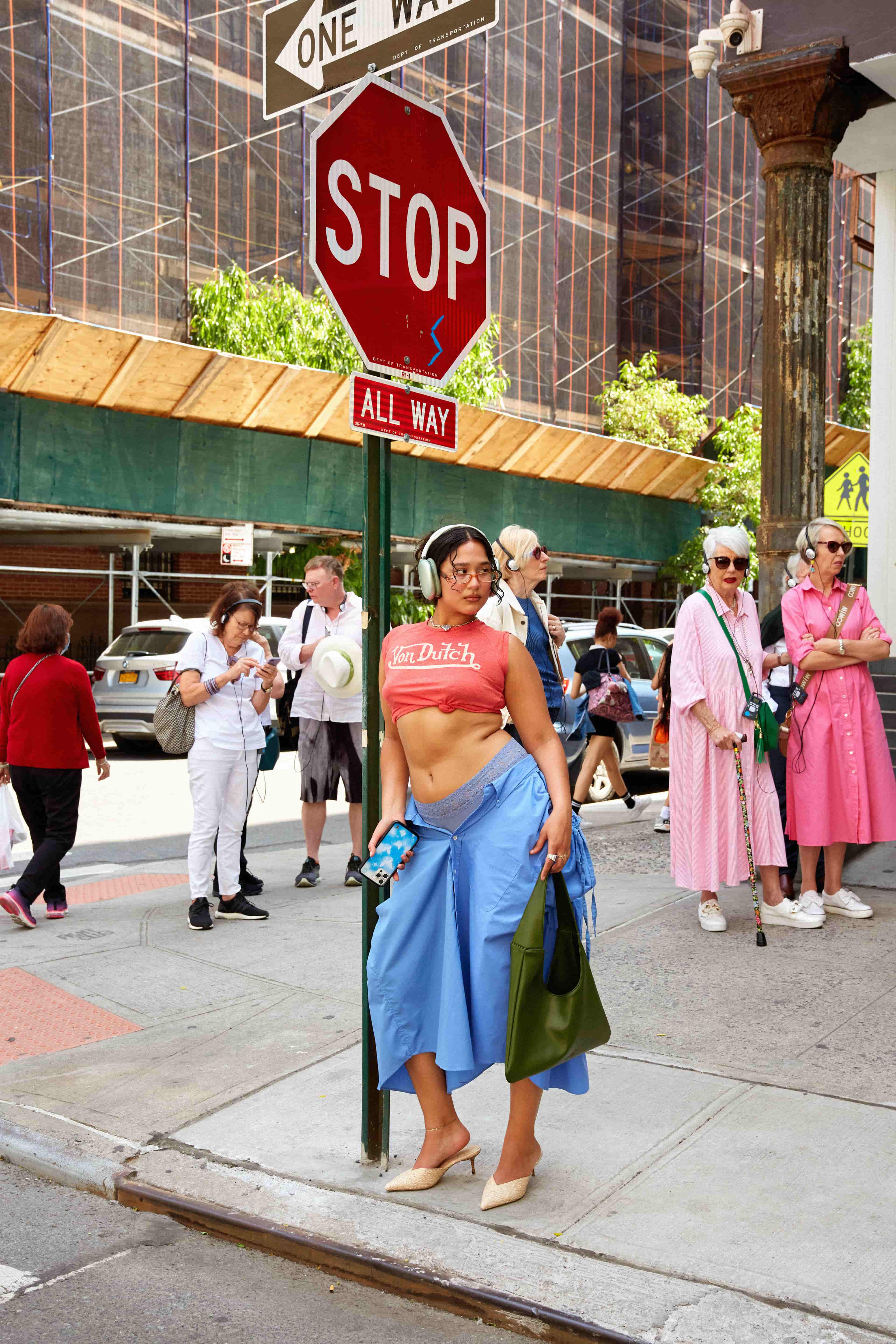Woman in colorful outfit standing on a city street corner in front of a stop sign holding a green tote bag made from cactus leather.