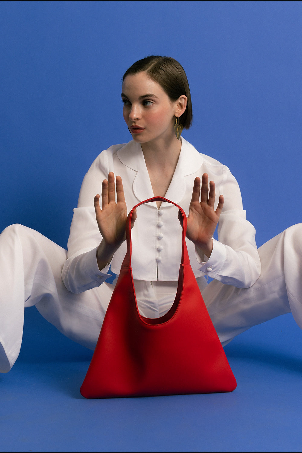 Woman in a white outfit holding a red handbag made of cactus leather against a blue background