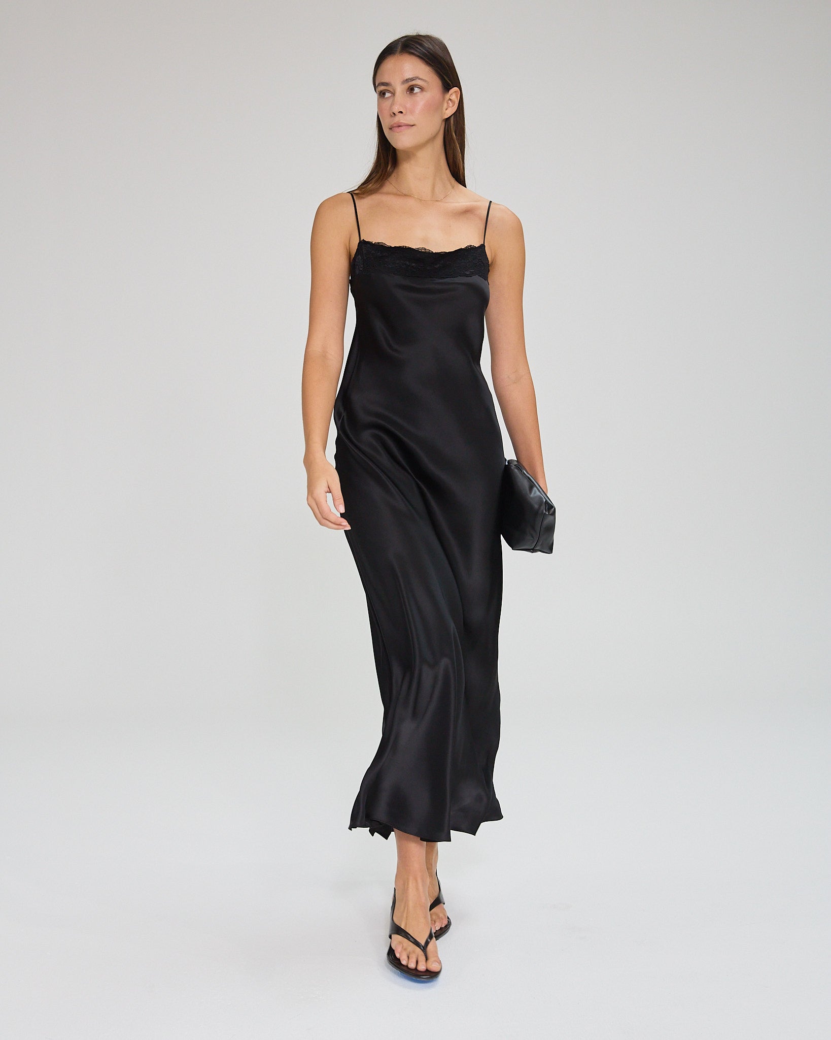 Model wearing a black, midi-length dress with two shoulder strap, featuring lace detail in a white background. Made from sustainable materials.