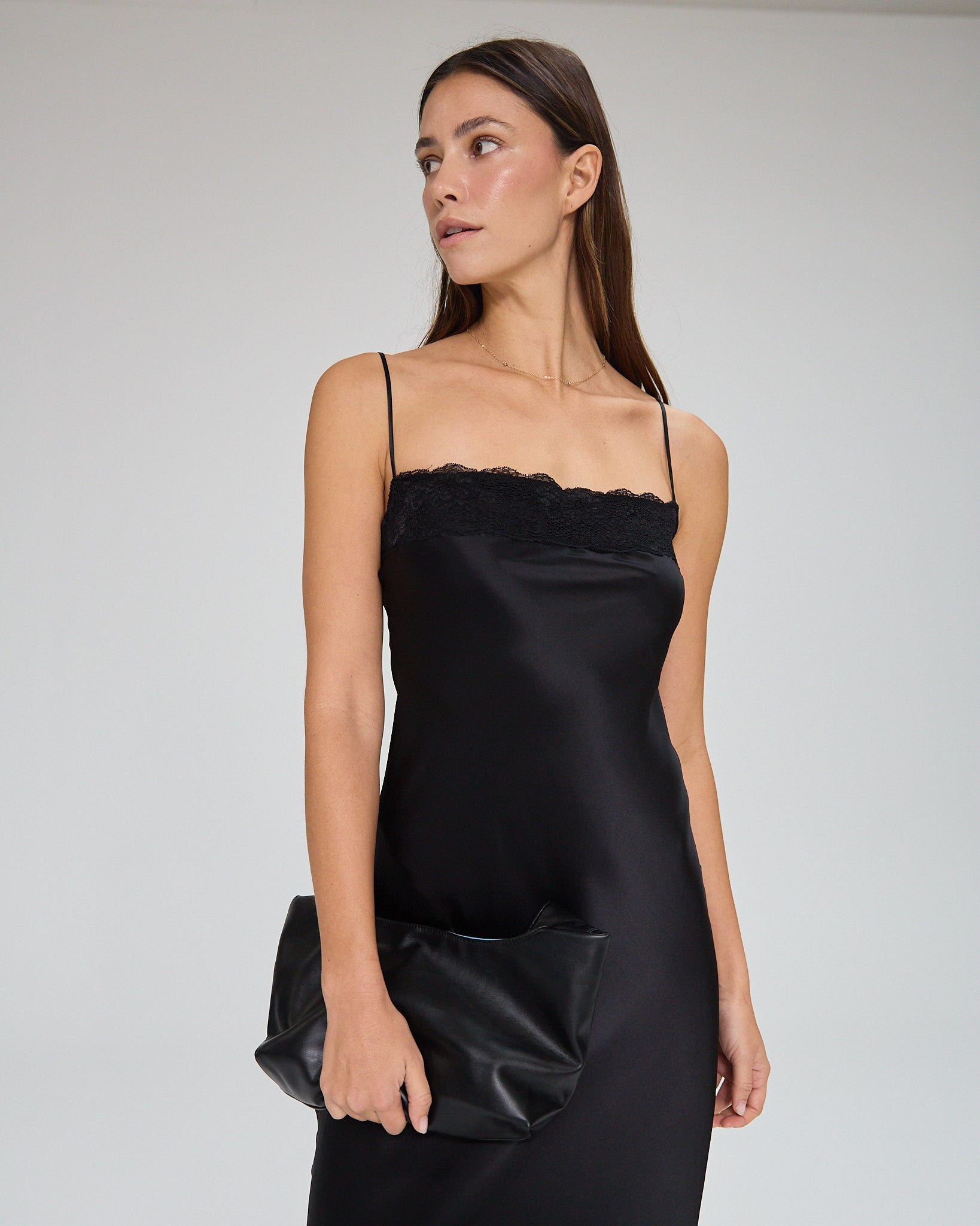 Model wearing a black, midi-length dress with two shoulder strap, featuring lace detail in a white background. Made from sustainable materials.