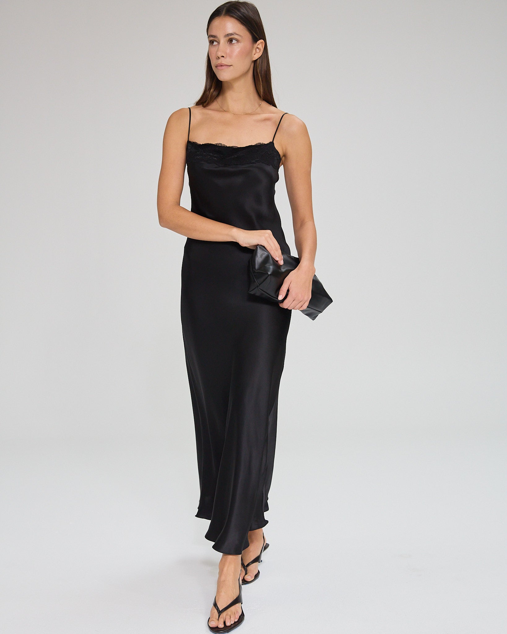 Model wearing a black, midi-length dress with two shoulder strap, featuring lace detail in a white background. Made from sustainable materials.