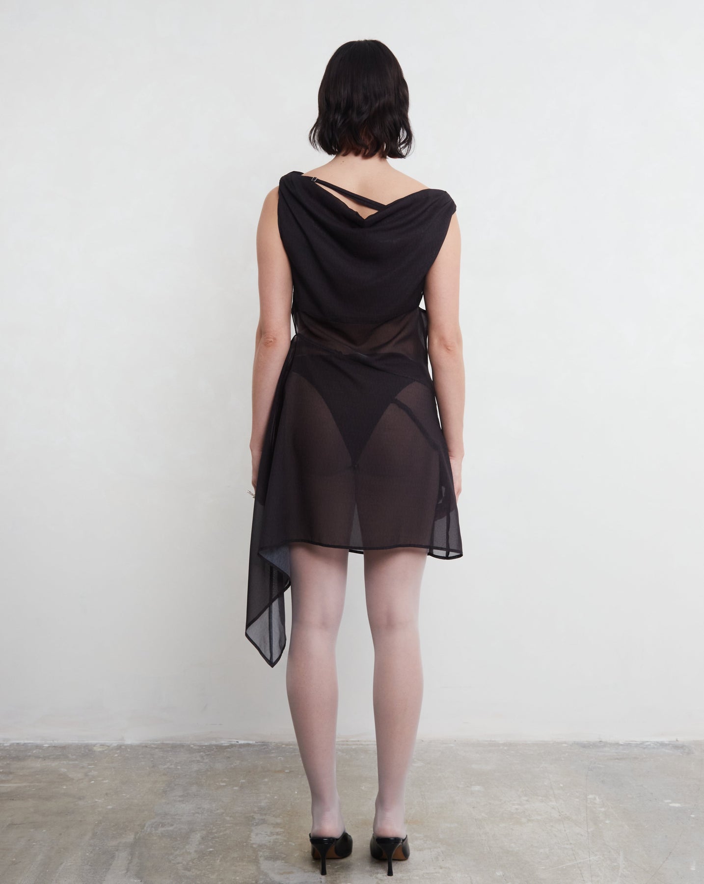 Model wearing a black dress with sheer panels against a white background. Made from sustainable deadstock materials.