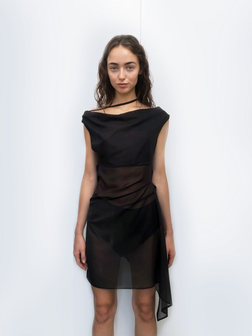 Woman wearing a sheer black dress against a white background. Made from sustainable deadstock materials.