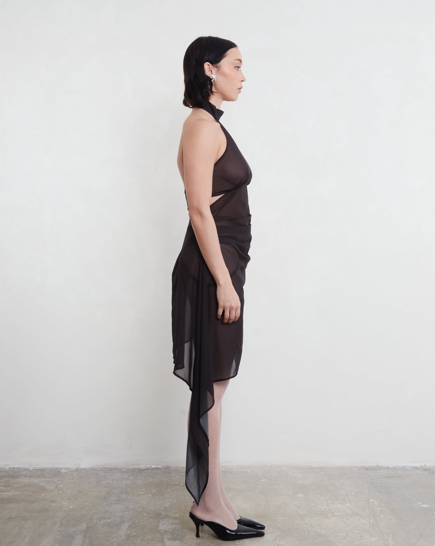 Woman wearing a black sustainable deadstock dress with a sheer overlay against a white background.