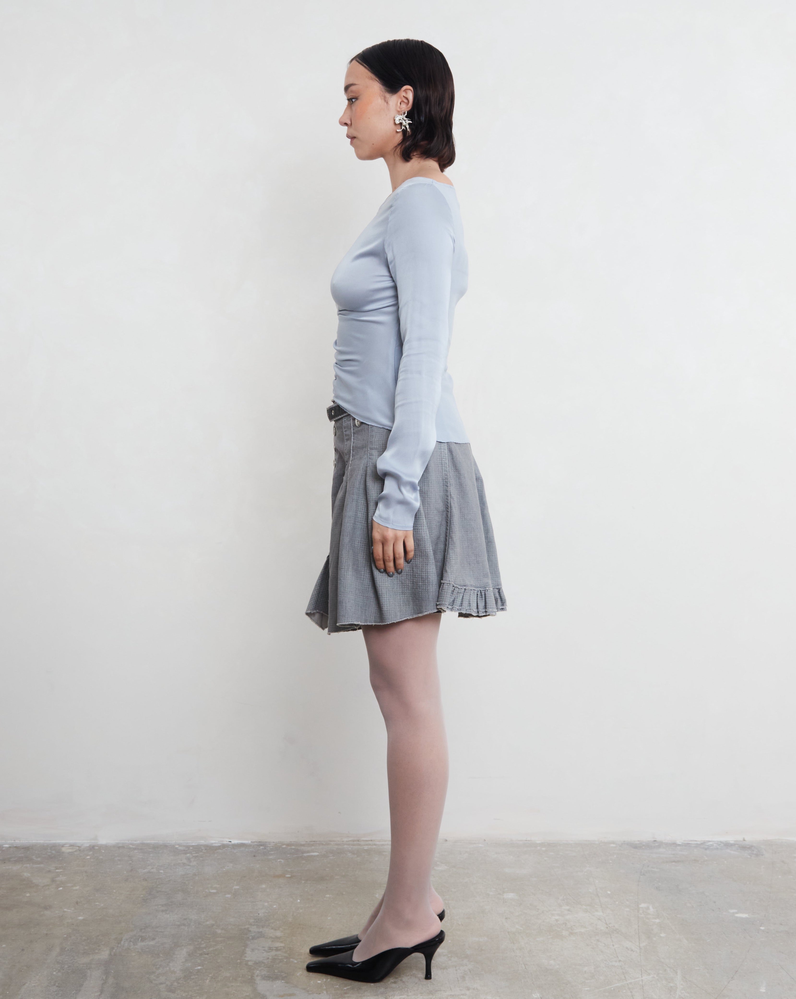 Woman wearing a light blue sustainable silk long-sleeve top and skirt against a white background.