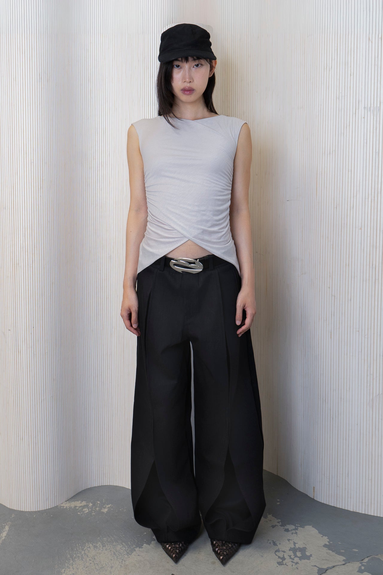 A woman wearing a boat-neck top with a subtle back cowl neckline, side ruching, and a high-low hemline in a bone color. Made from 100% deadstock fabric. Front View.