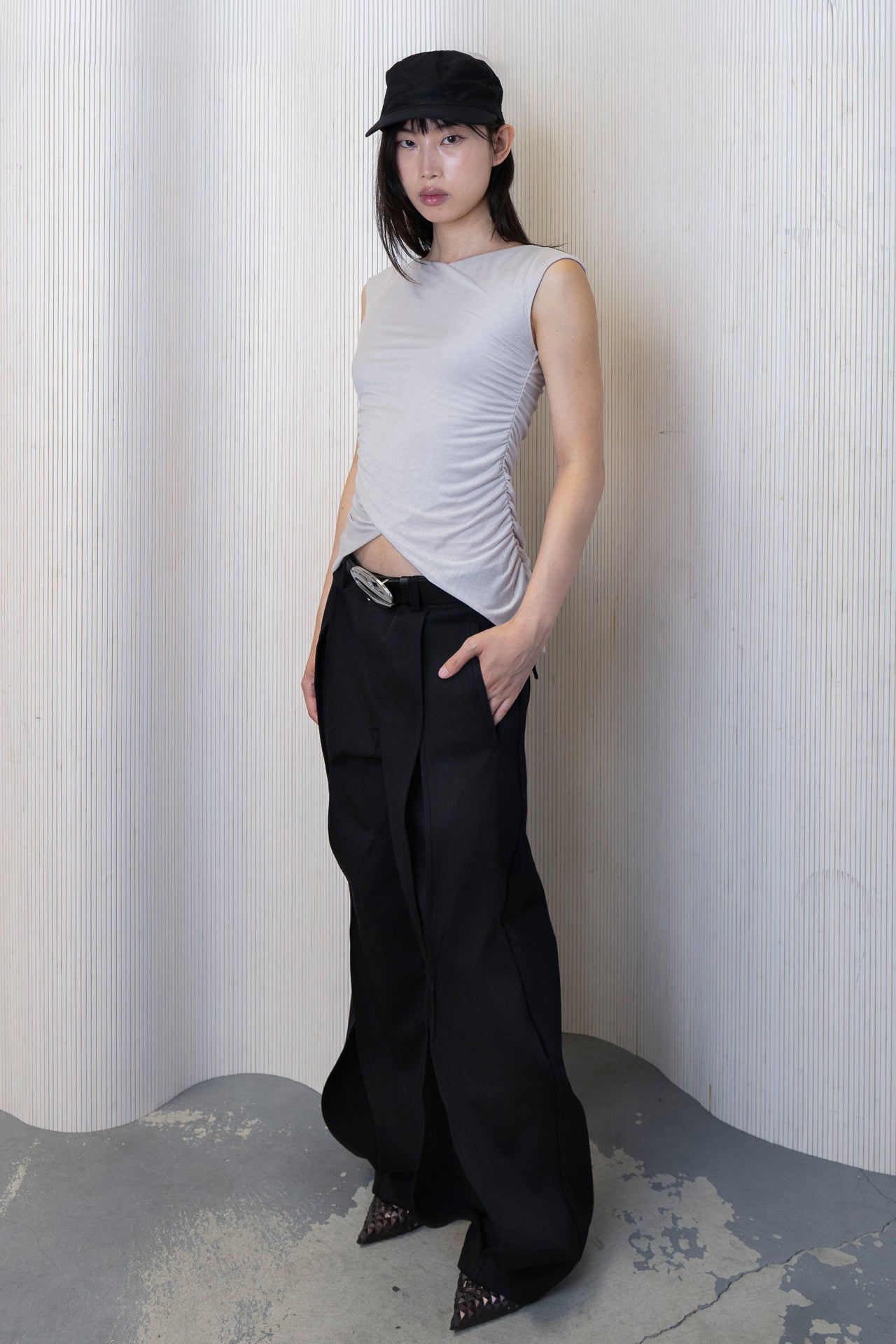Model wearing a boat-neck top with a subtle back cowl neckline, side ruching, and a high-low hemline in a bone color. Made from 100% deadstock fabric.