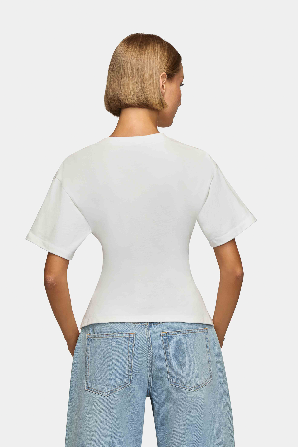 Woman wearing a white, oversized tee with short sleeves and a round neckline. Made from 100% Organic Cotton. Back View.