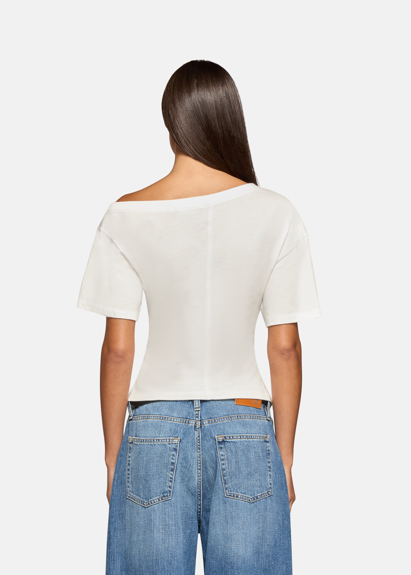 A model wearing the white elena off shoulder tee in a white background. 100% made from cotton.
