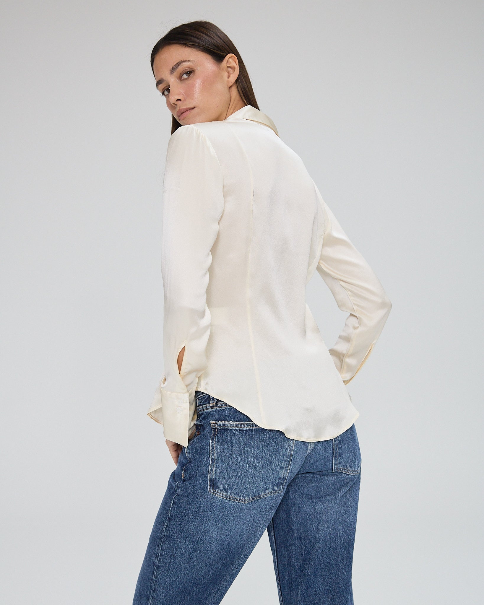 Model wearing a silk butter long sleeve button up blouse in a white background. Made from sustainable materials.
