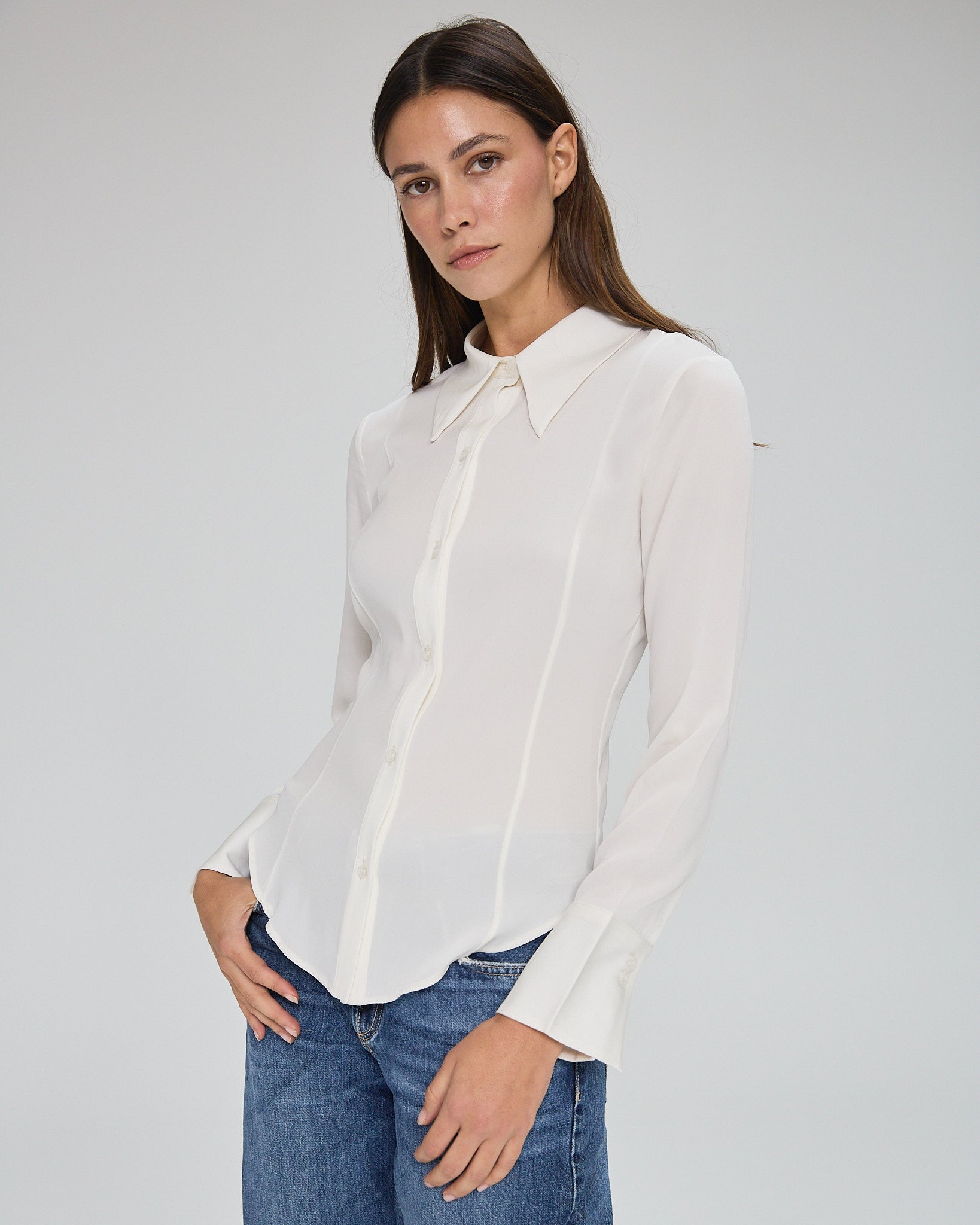 Model wearing a silk ivory long sleeve button up blouse in a white background. Made from sustainable materials.
