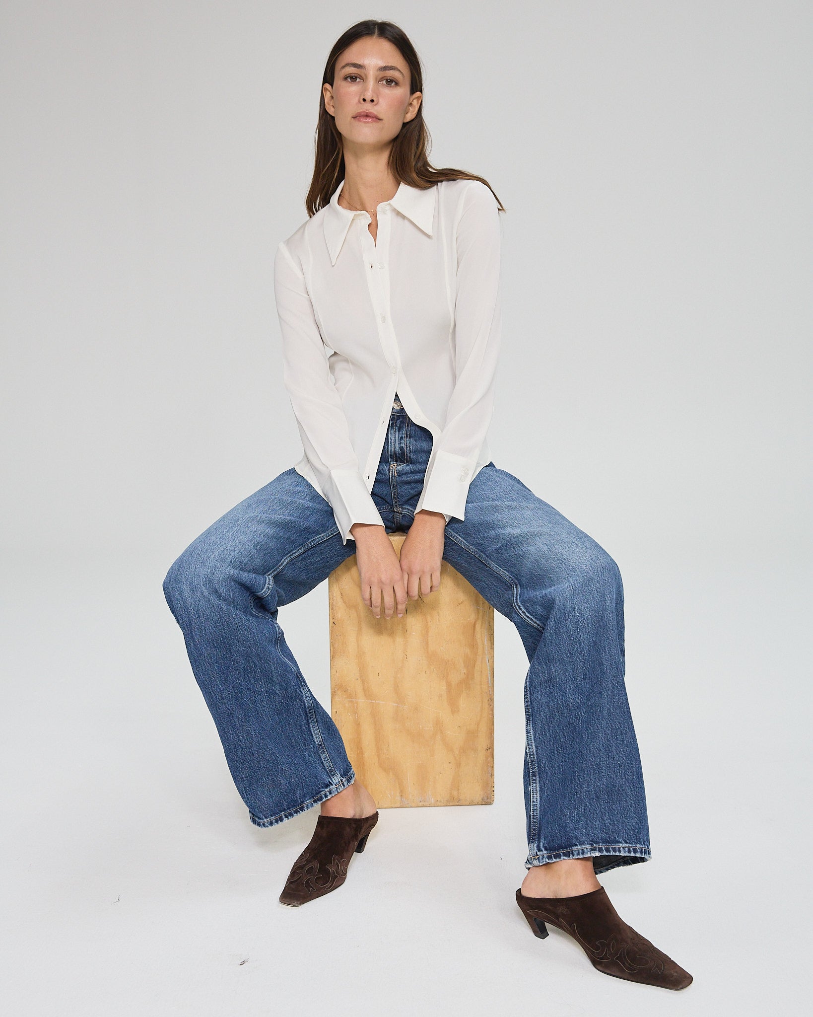 Model wearing a silk ivory long sleeve button up blouse in a white background. Made from sustainable materials.