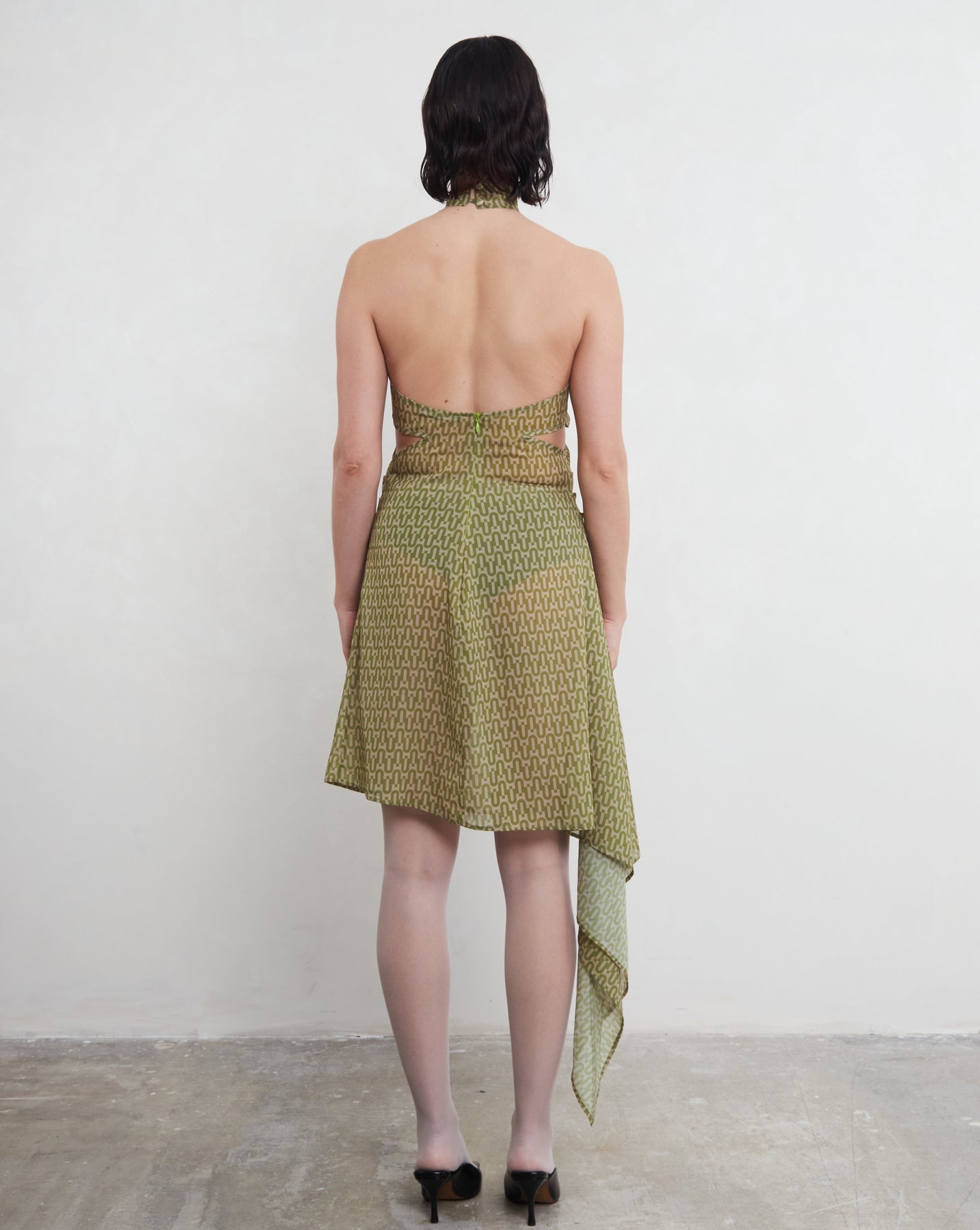Woman wearing a green dress with a patterned design, standing against a white background. Made from sustainable, deadstock materials.