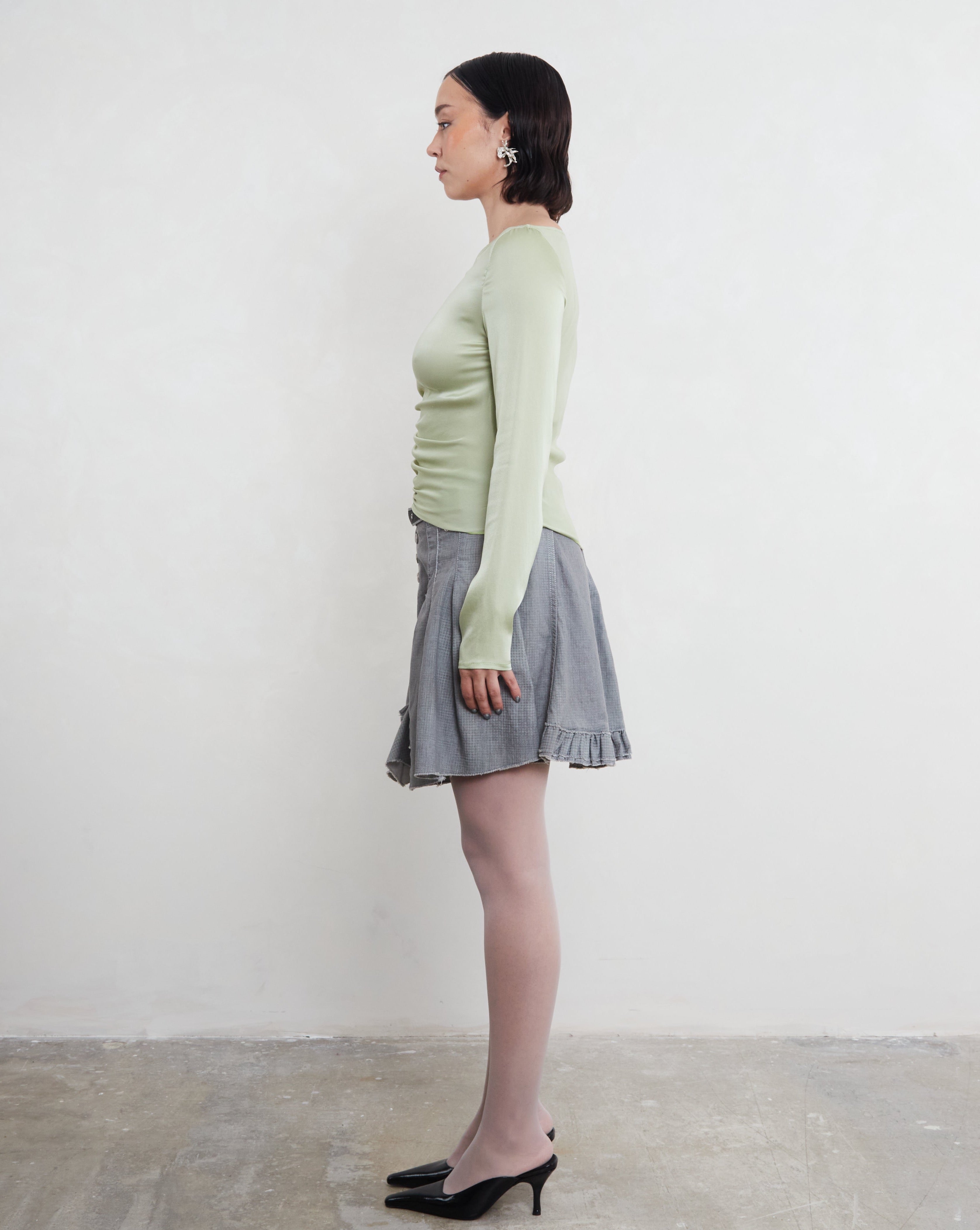 Woman wearing a light green long-sleeve top and gray skirt against a plain background. Made from sustainable silk.