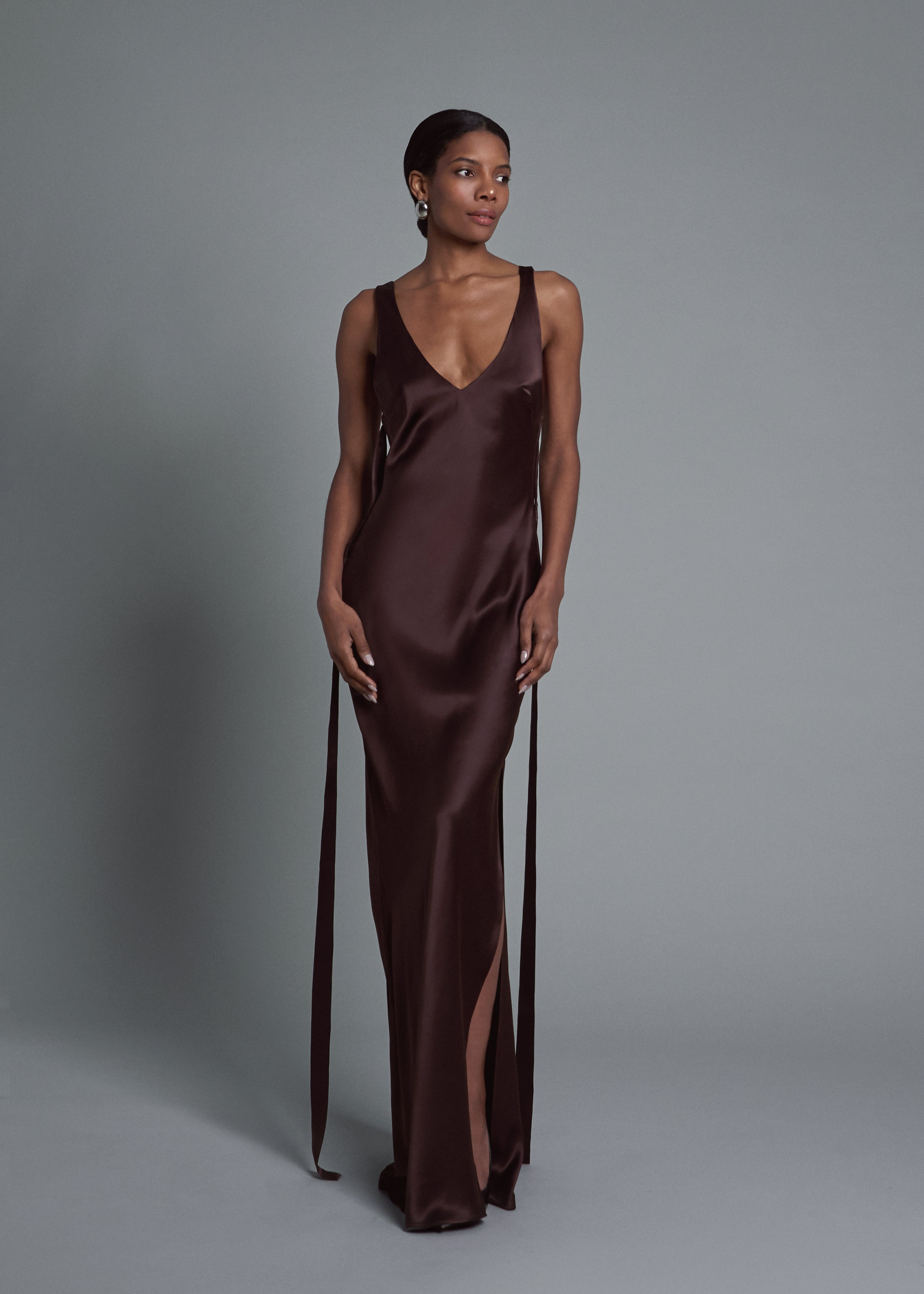 A model wearing the gaia gown in choco in a white background. Crafted from 100% silk satin.