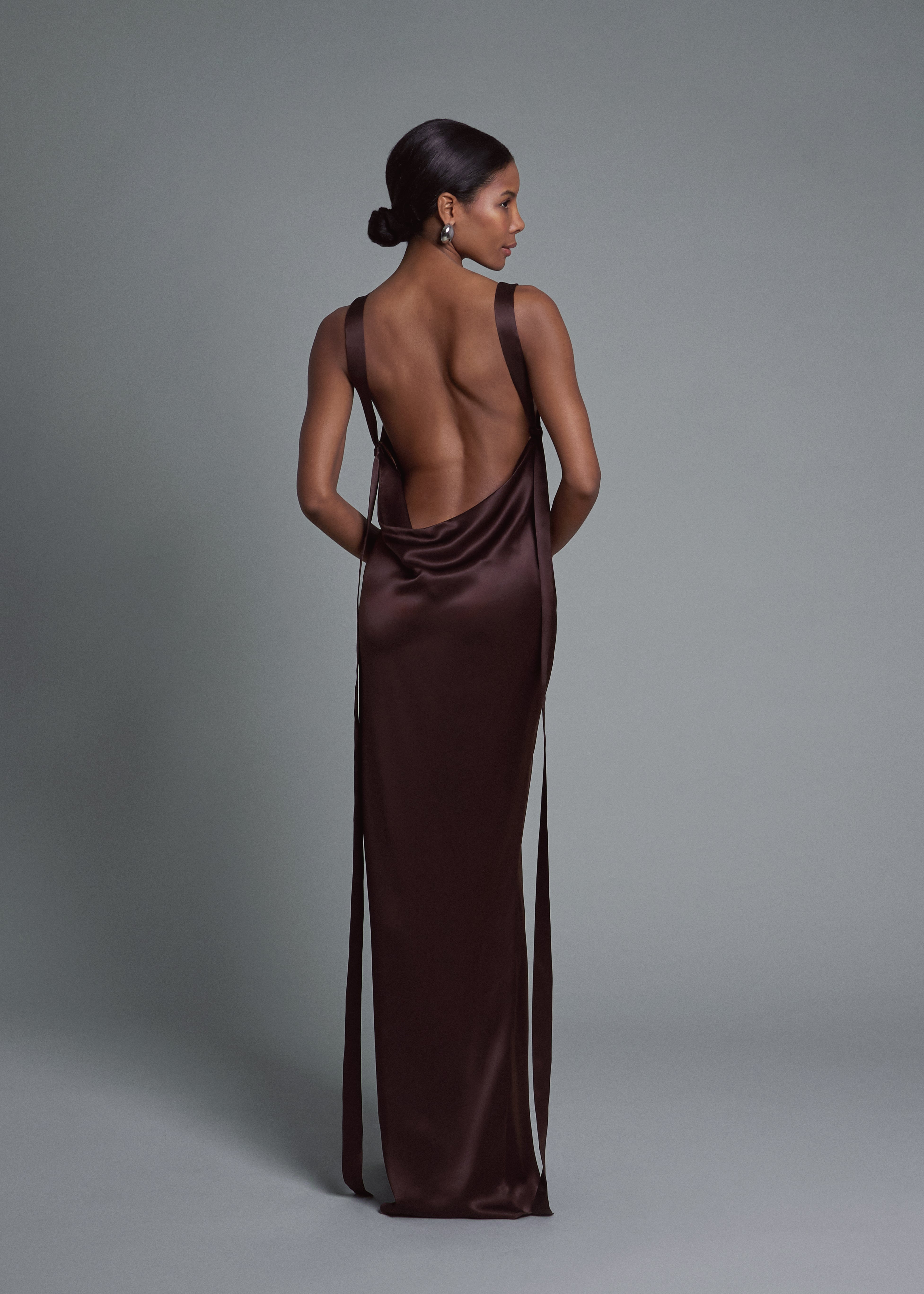 A model wearing the gaia gown in choco in a white background. Crafted from 100% silk satin.