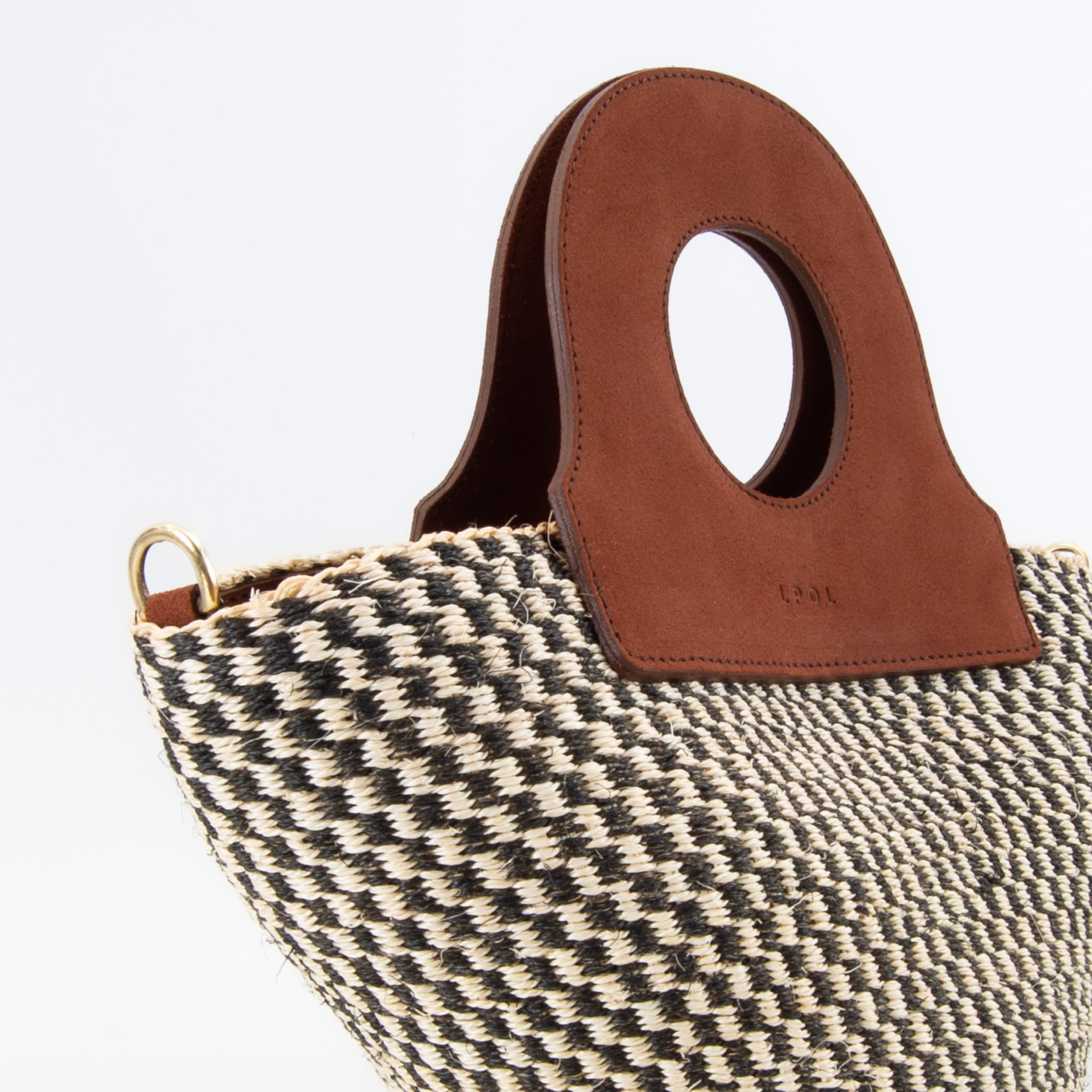 The handheld basket bag in a white background. Handwoven sisal basket made in Kenya. Finished in England using chrome-free leather. CLOSE-UP