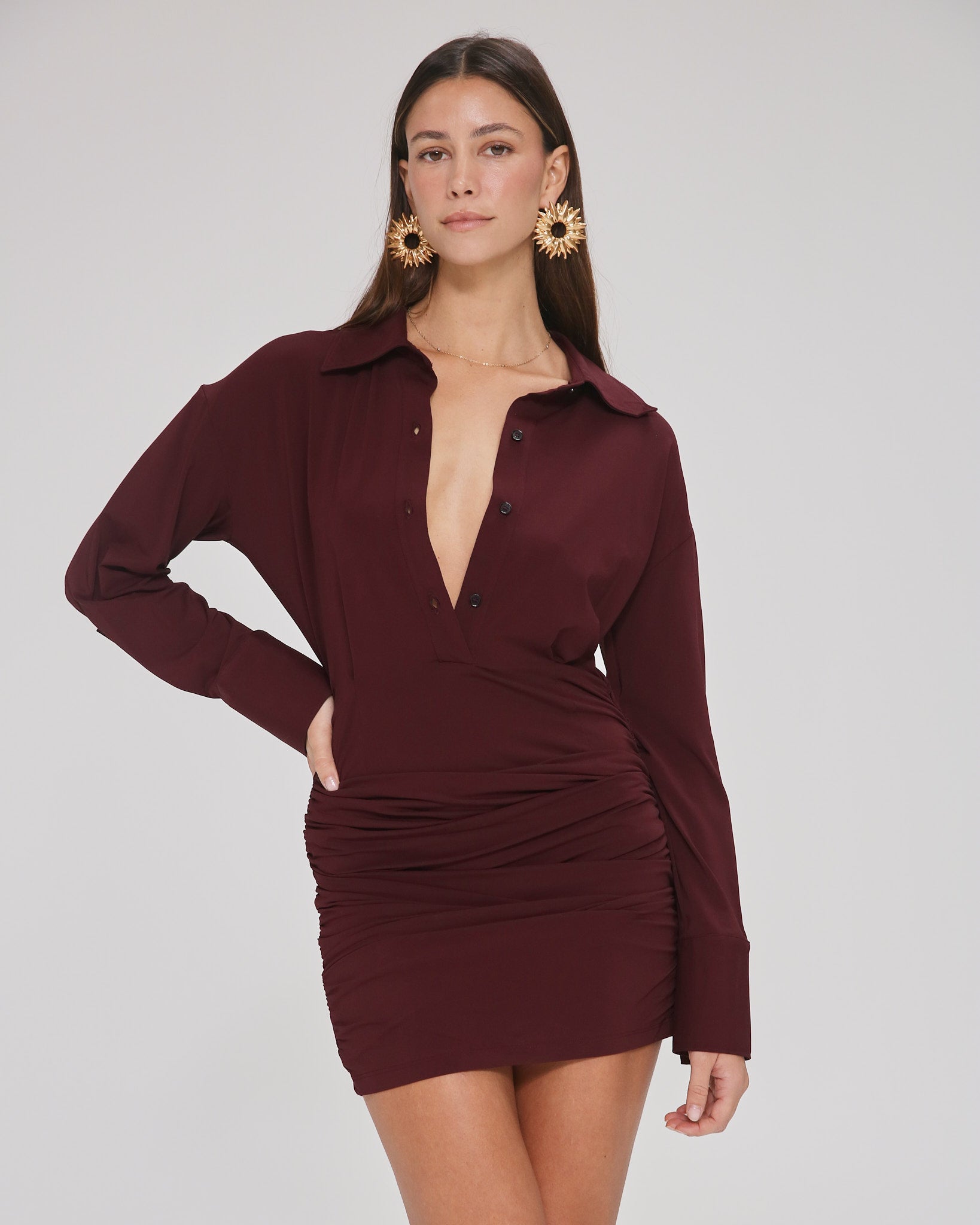 Model wearing a burgundy, mini-length long sleeve dress with buttons and collar in a white background. Made from sustainable deadstock materials.