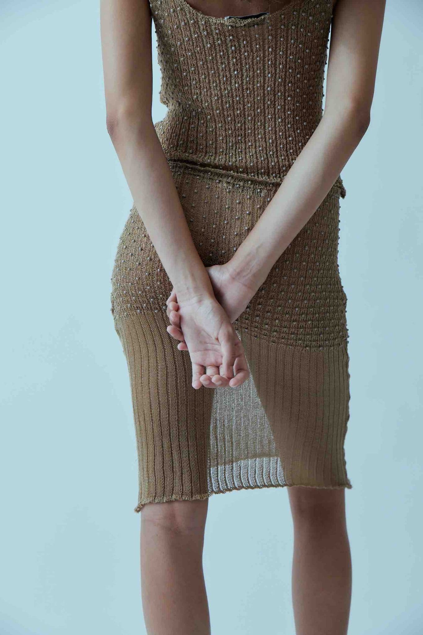 A model wearing the kie top in a white background. 100% beige cotton knit.