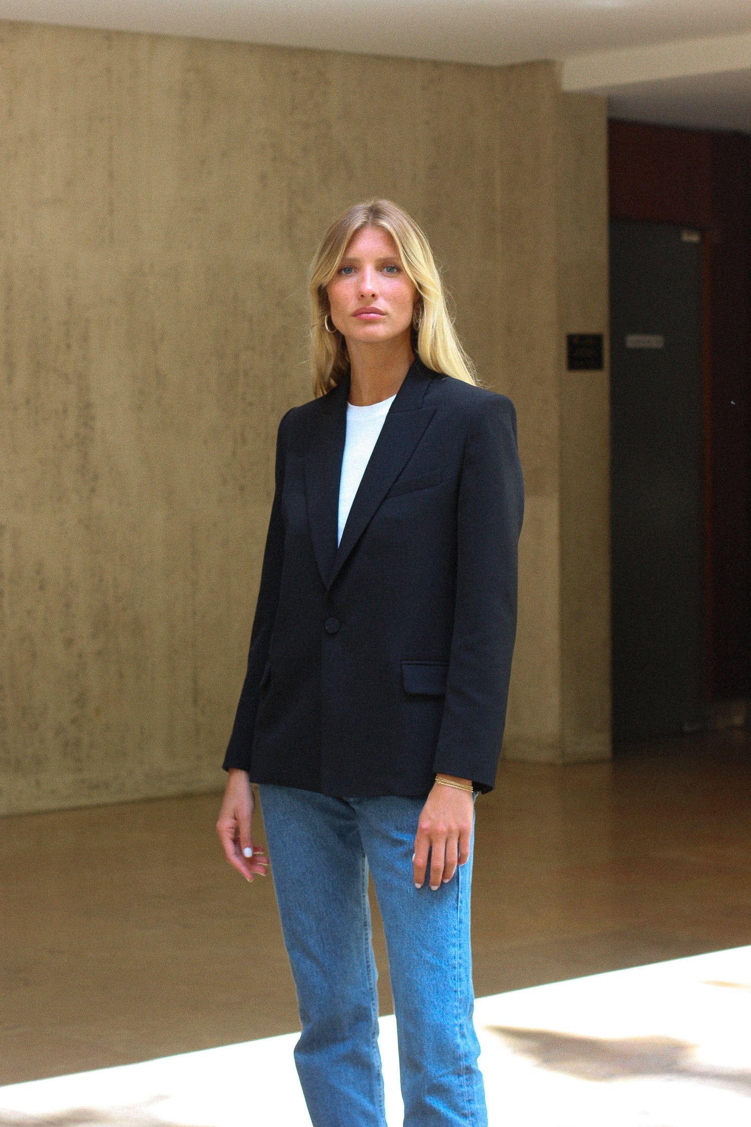 A model wearing the lauren black wool gabardine blazer in an aesthetically background. 100% made from sustainable upcycled wool.