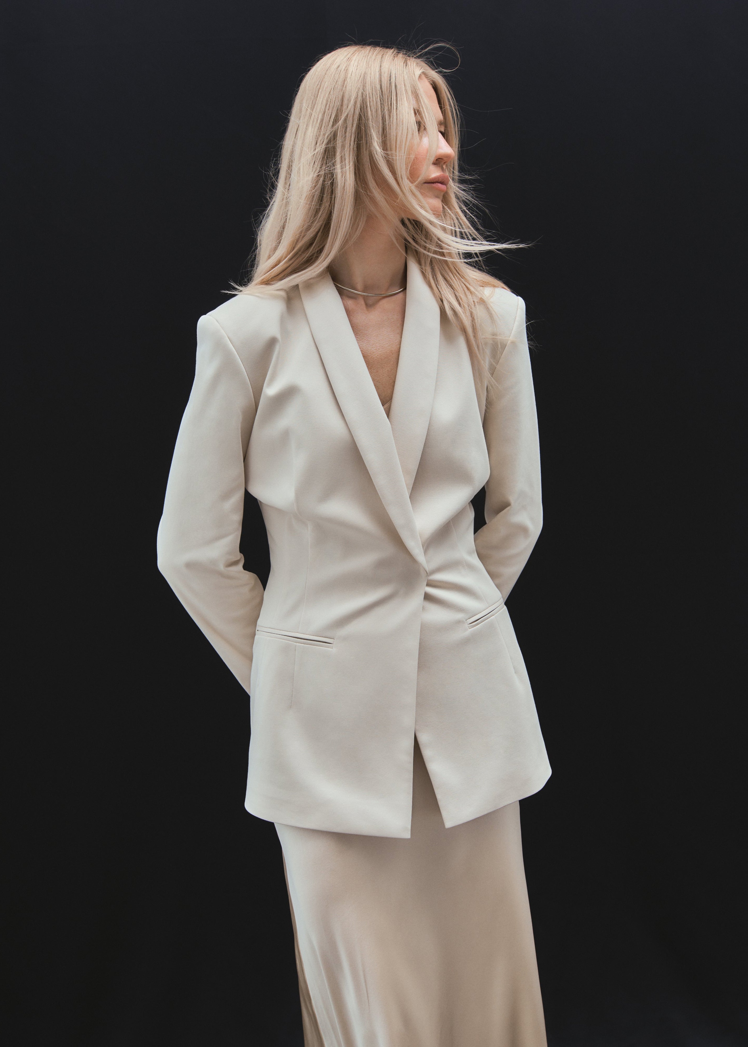A model posing wearing a light beige organic cotton sustainable blazer with fitted waist and hidden pockets