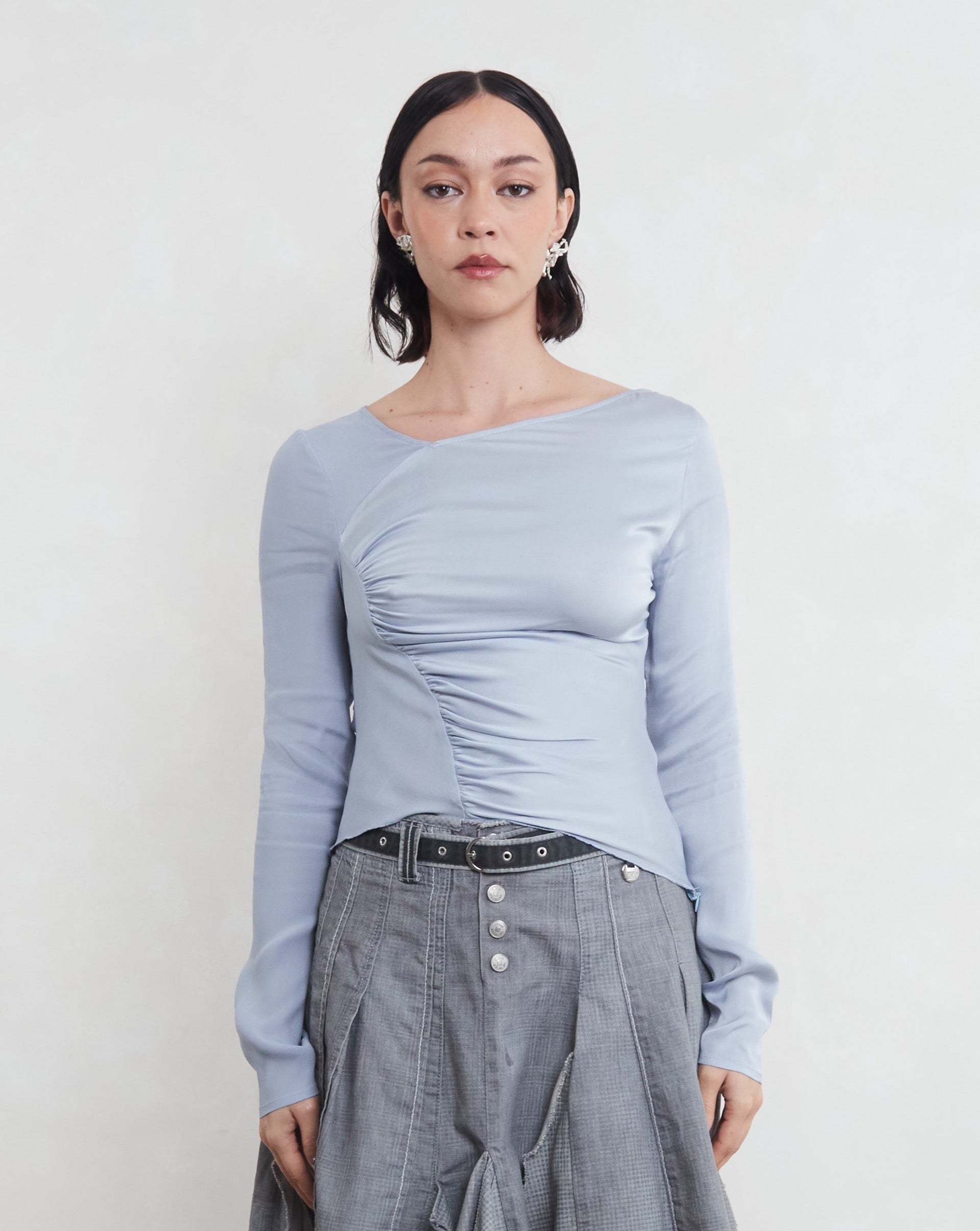 Woman wearing a light blue sustainable silk long-sleeve top against a plain background