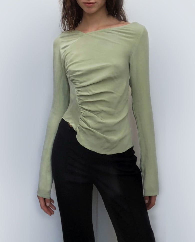 Woman wearing a light green sustainable long-sleeve top against a plain background