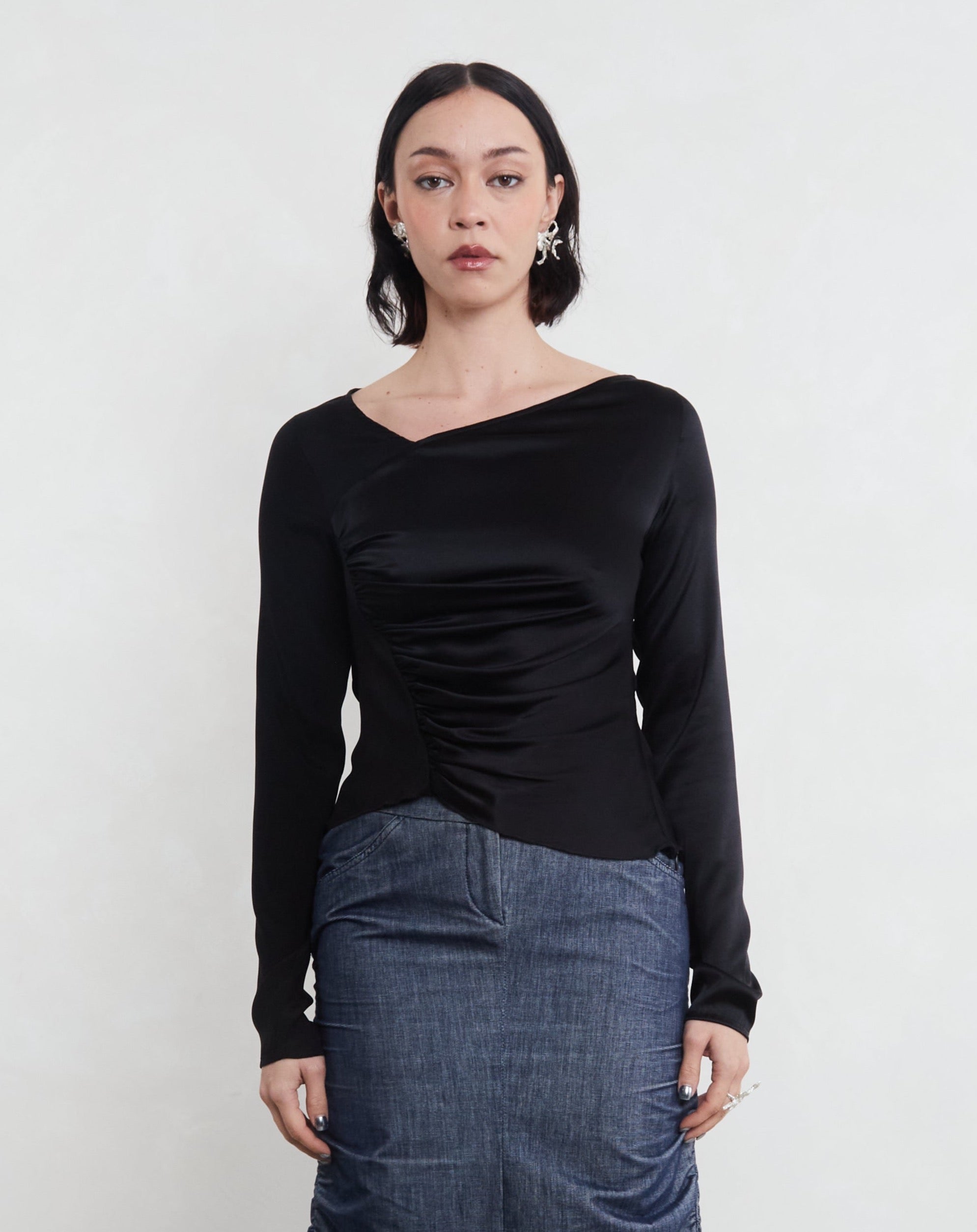 Woman wearing a sustainable silk black long-sleeve top and blue skirt on a white background