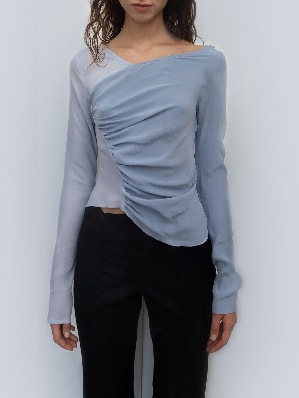 Woman wearing a light blue sustainable silk long-sleeve top with a ruched design.