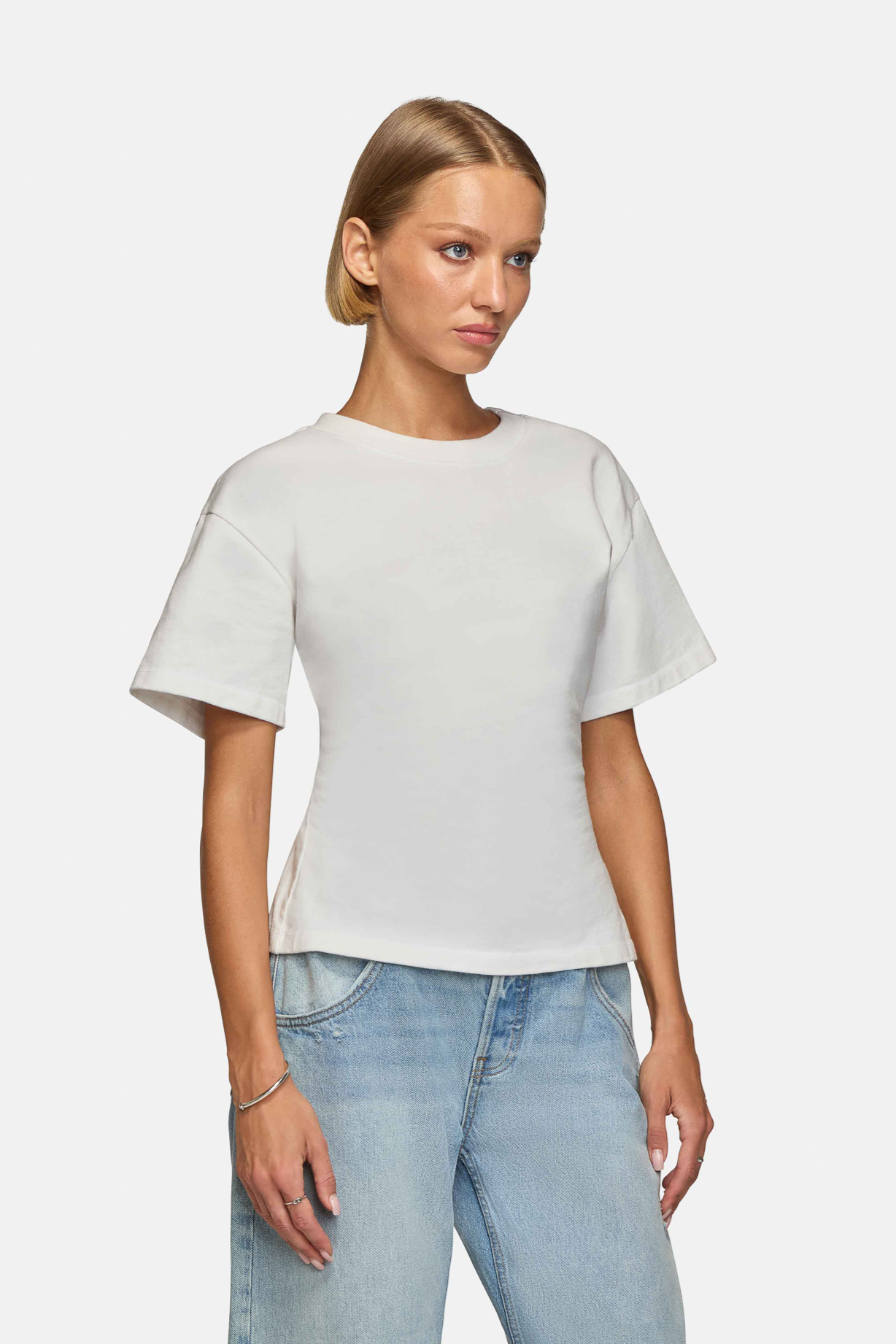 Woman wearing a white, oversized tee with short sleeves and a round neckline. Made from 100% Organic Cotton. Side view.