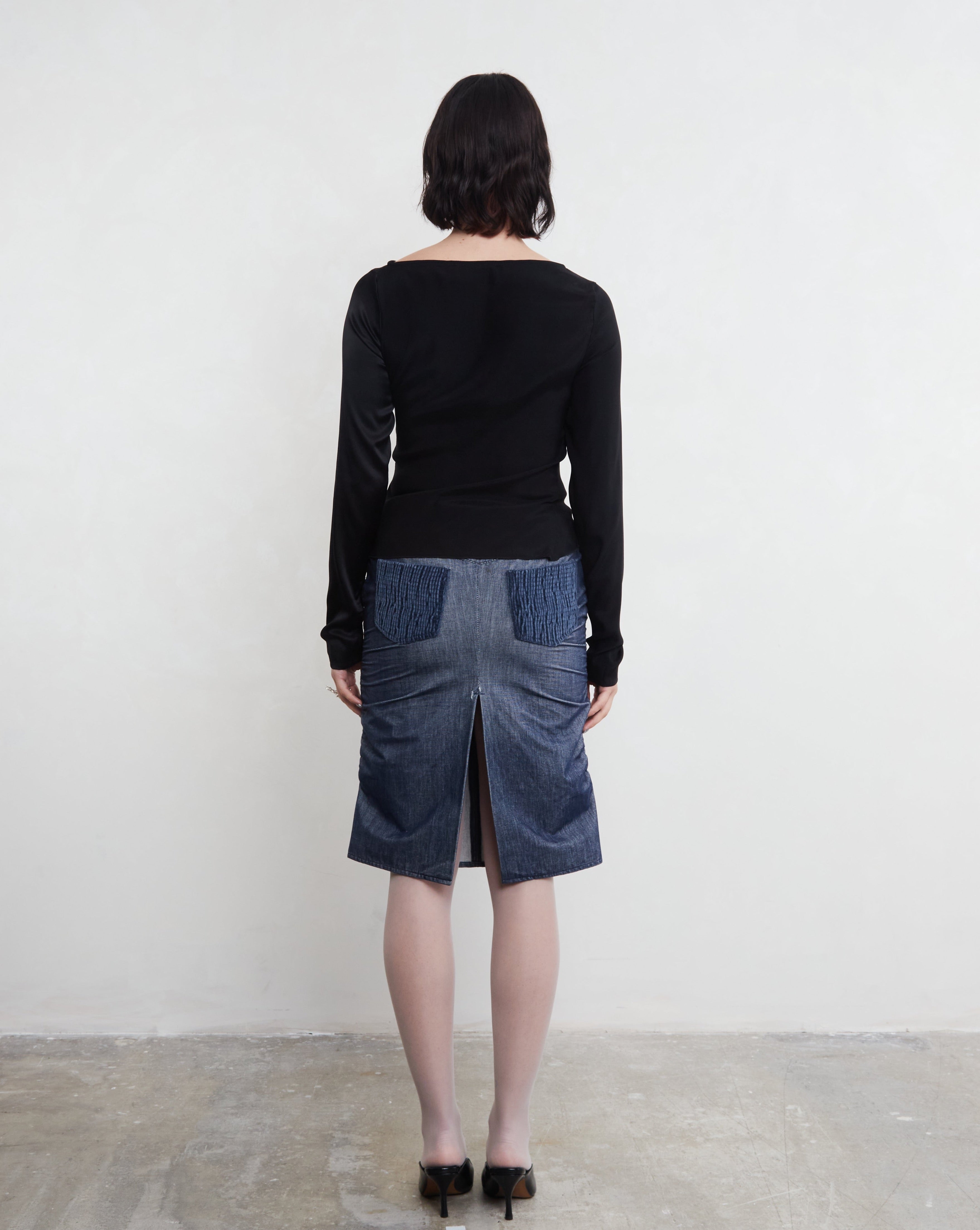 Woman wearing a black sustainable silk top and blue denim skirt against a white background.