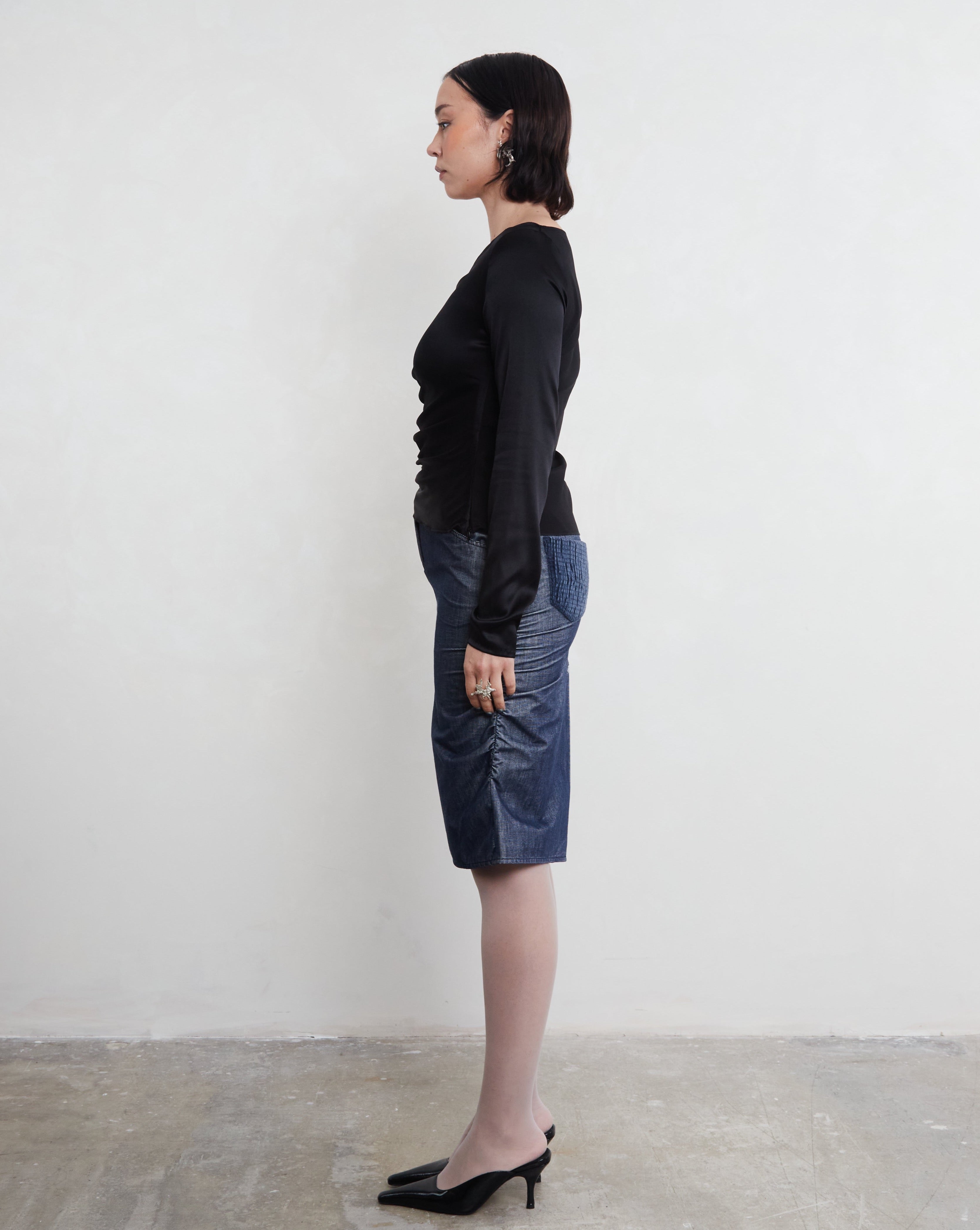 Woman wearing a sustainable silk black top and blue skirt against a white background