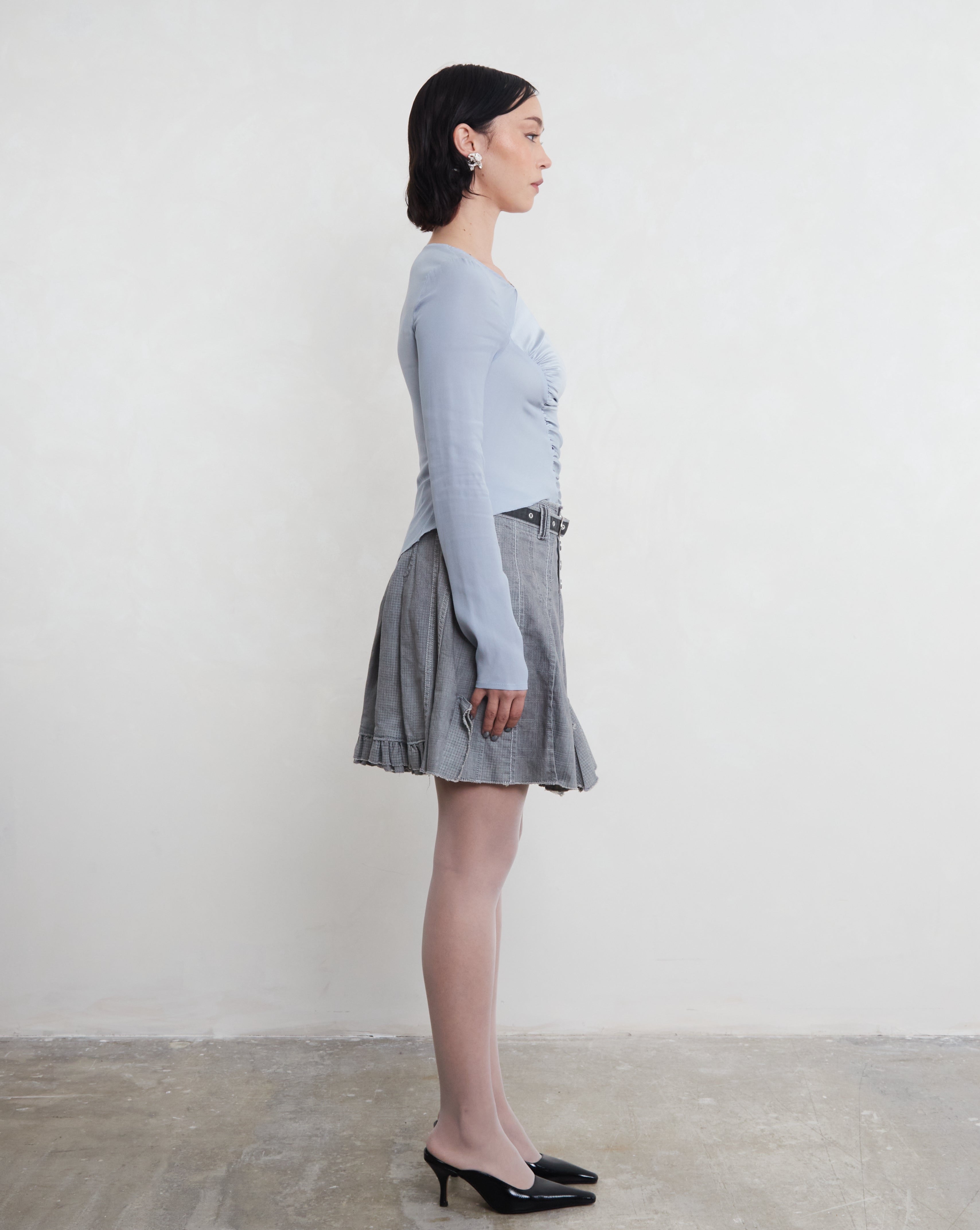 Woman wearing a blue long-sleeve top and plaid skirt standing against a white background. Top is made from sustainable silk.