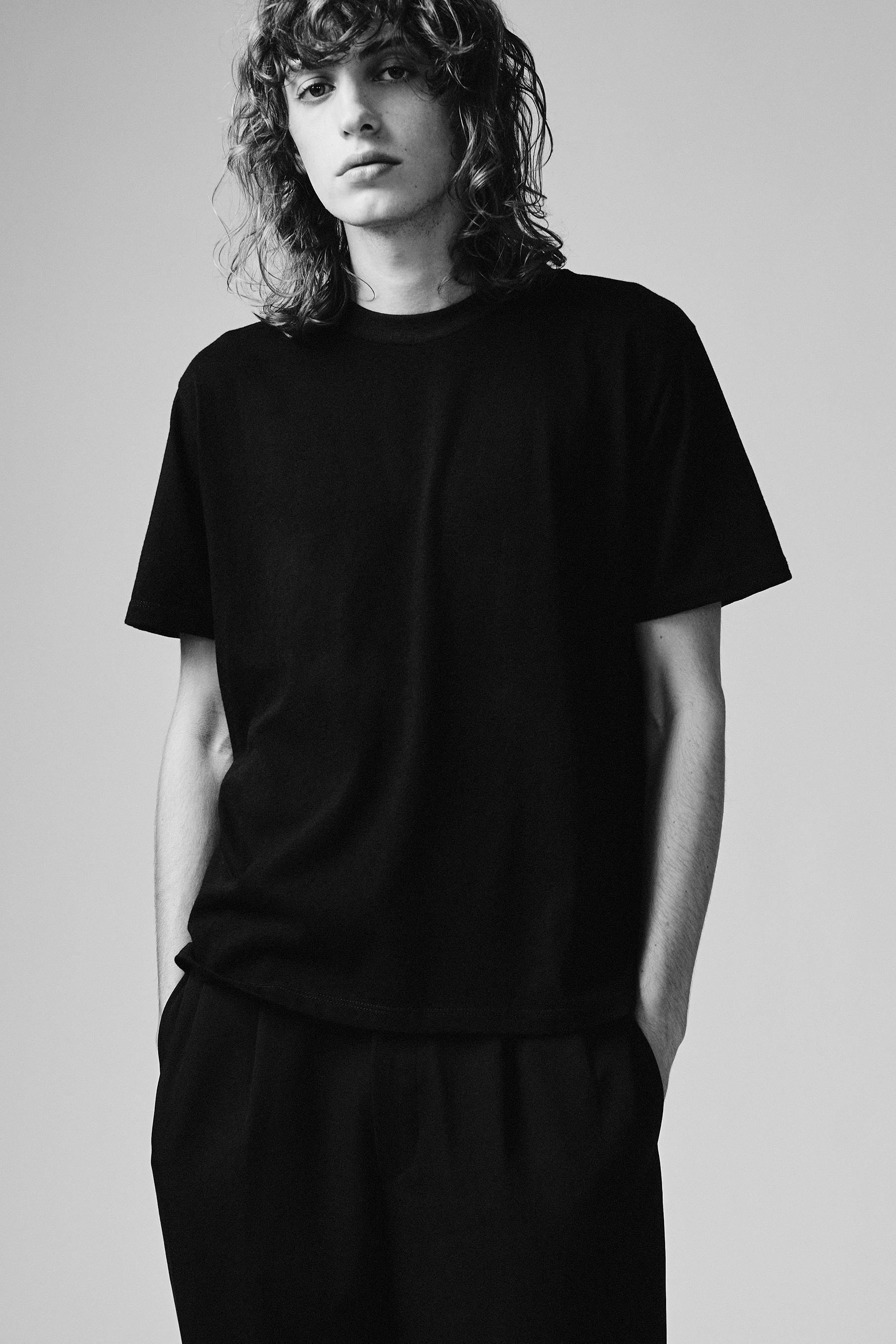 A model wearing the black T101 classic tee in a white background. 100% made from organic grown cotton.