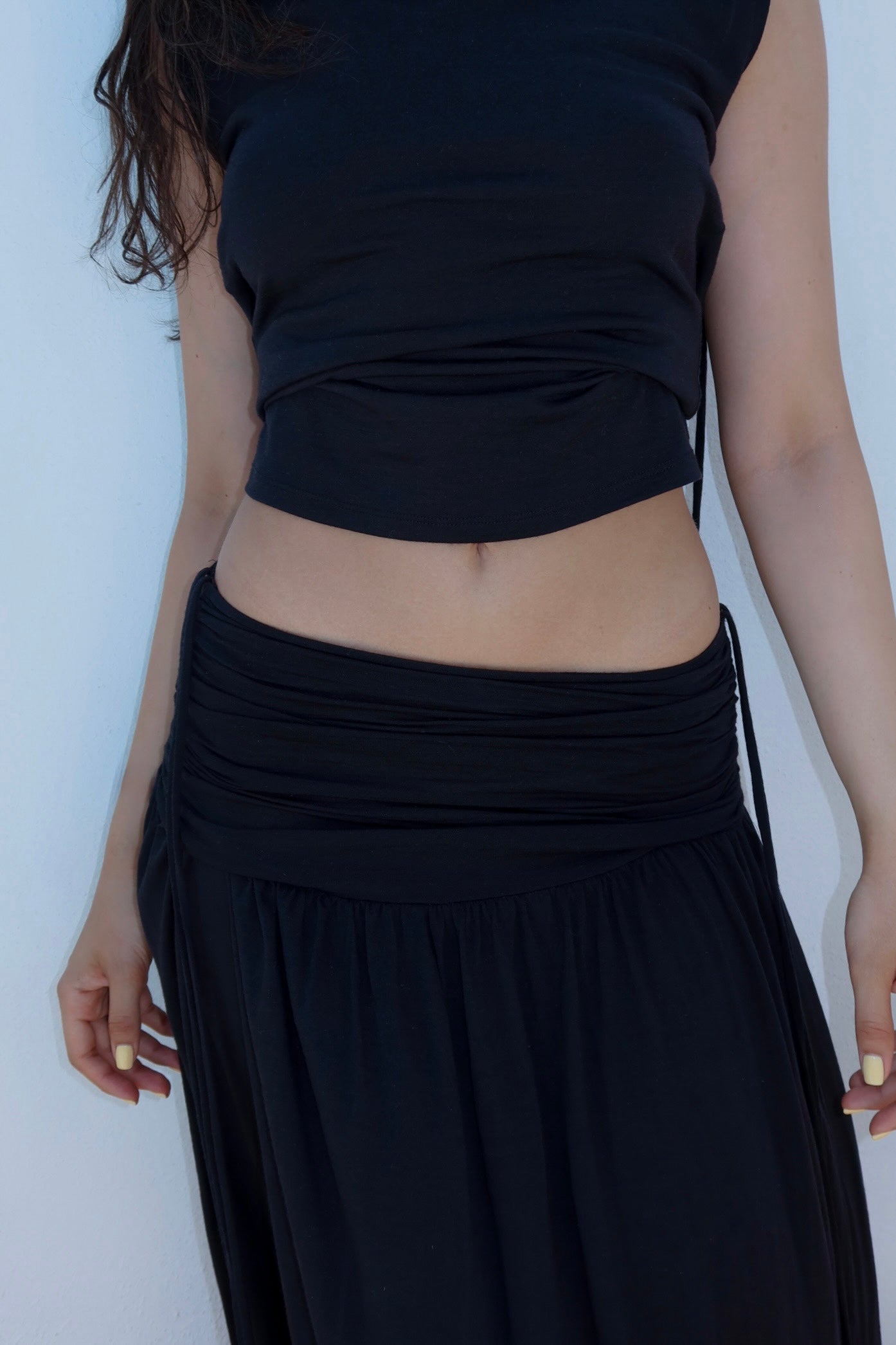 Woman wearing a black sustainable sleeveless top and black skirt against a white background