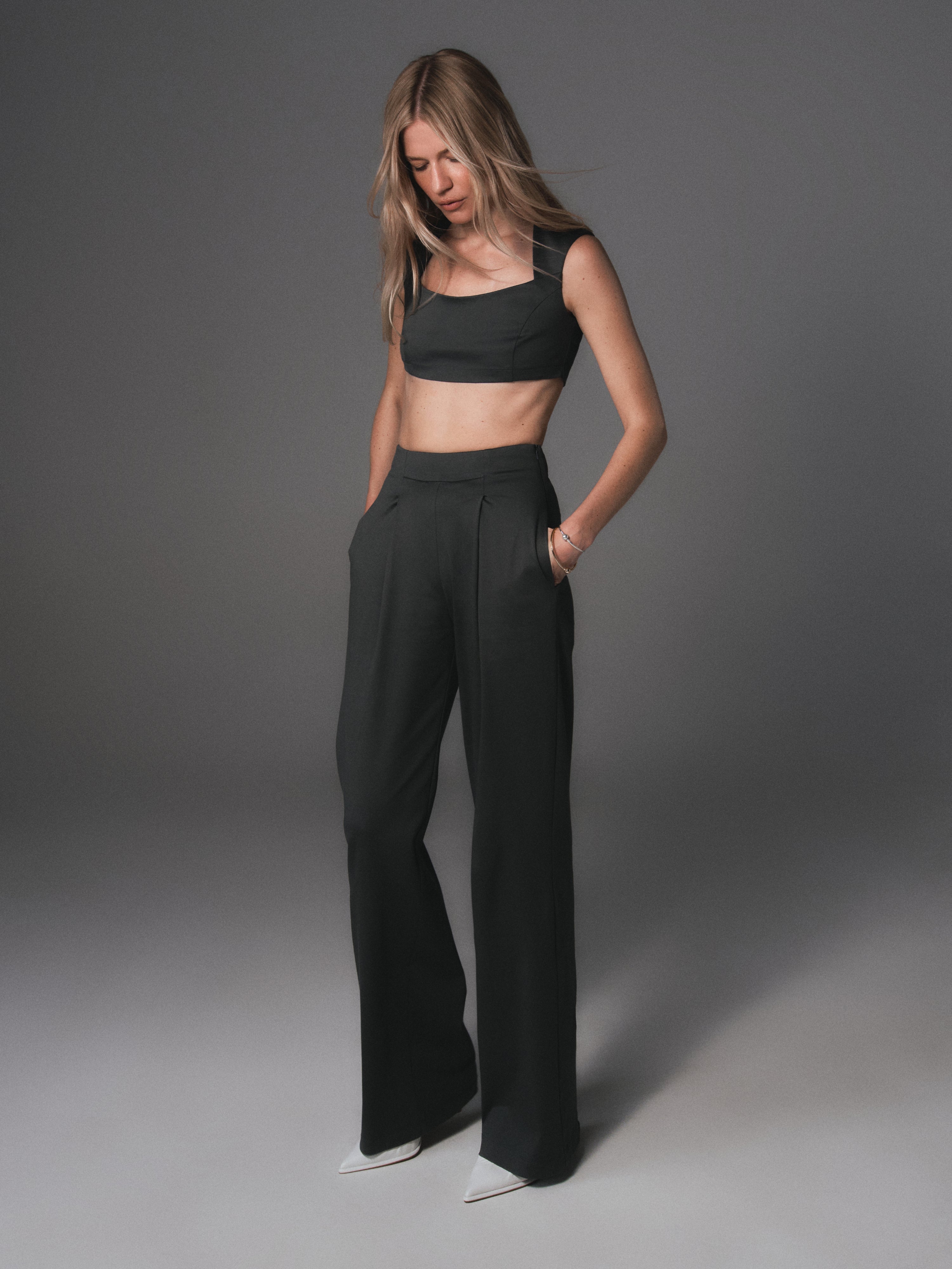 A model posing in a set of a crop top and high waisted pants created from organic 100% cotton in color dark grey