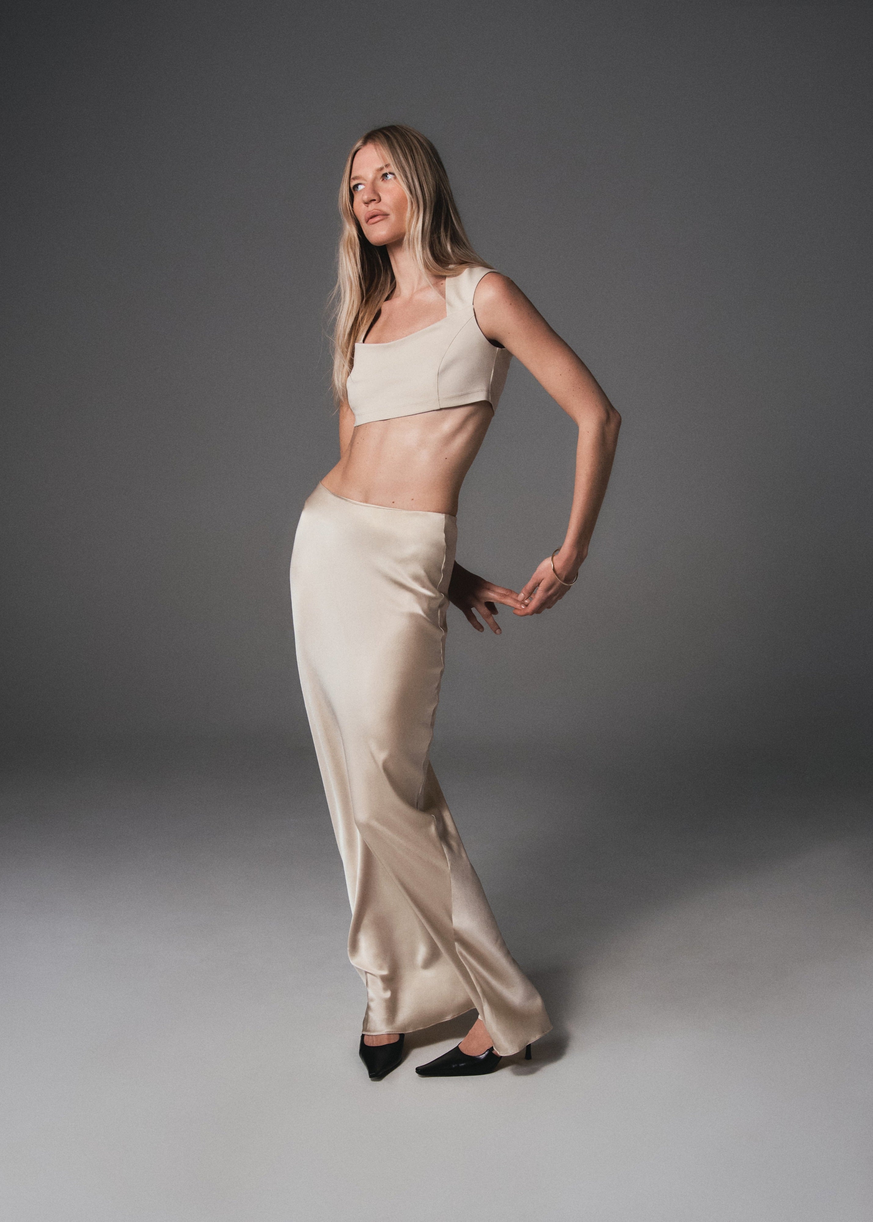 A model posing in a crop top made from organic cotton and a silk maxi skirt in light beige color