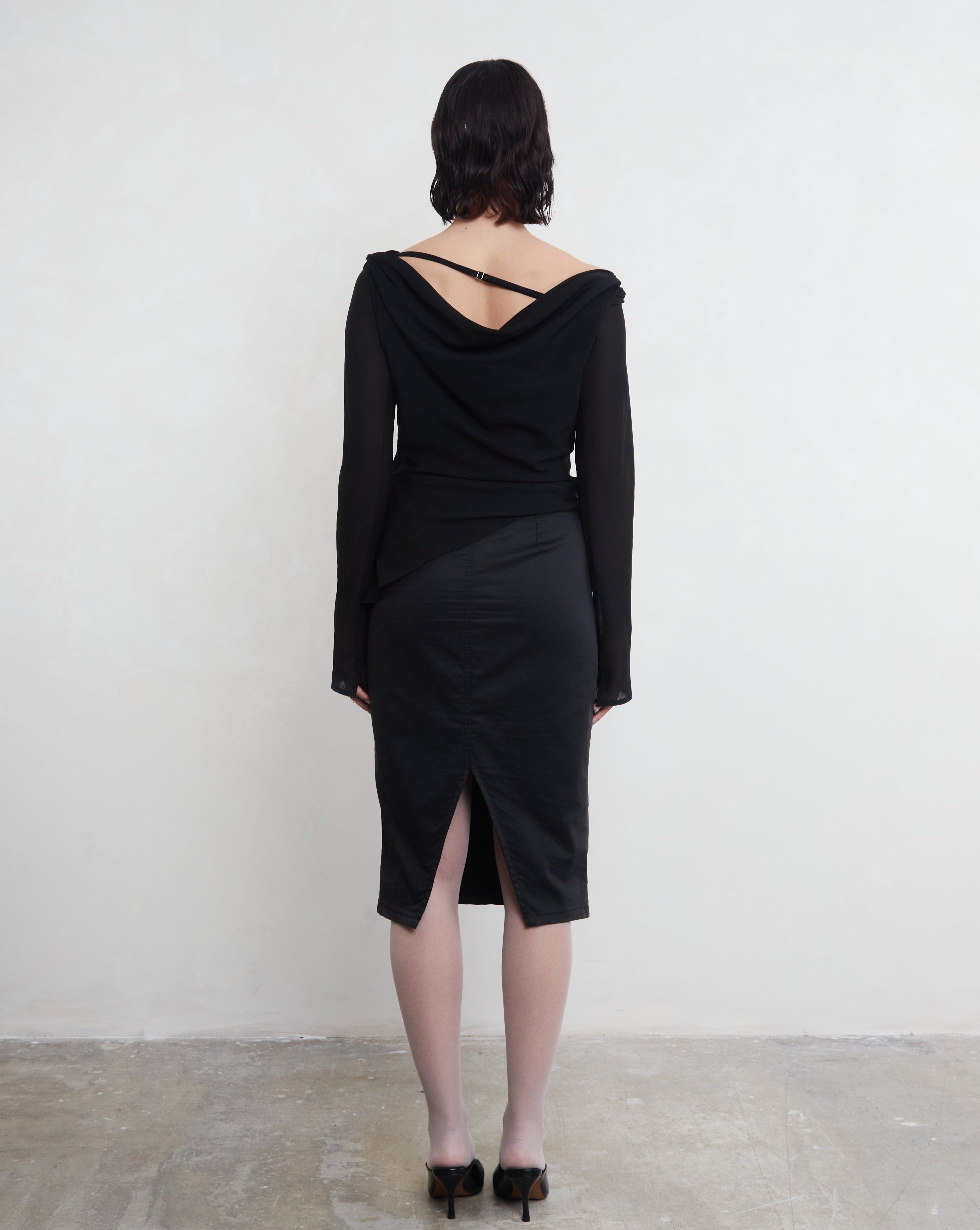Person wearing a black dress with a backless design against a white background. Made from 100% recycled material. 