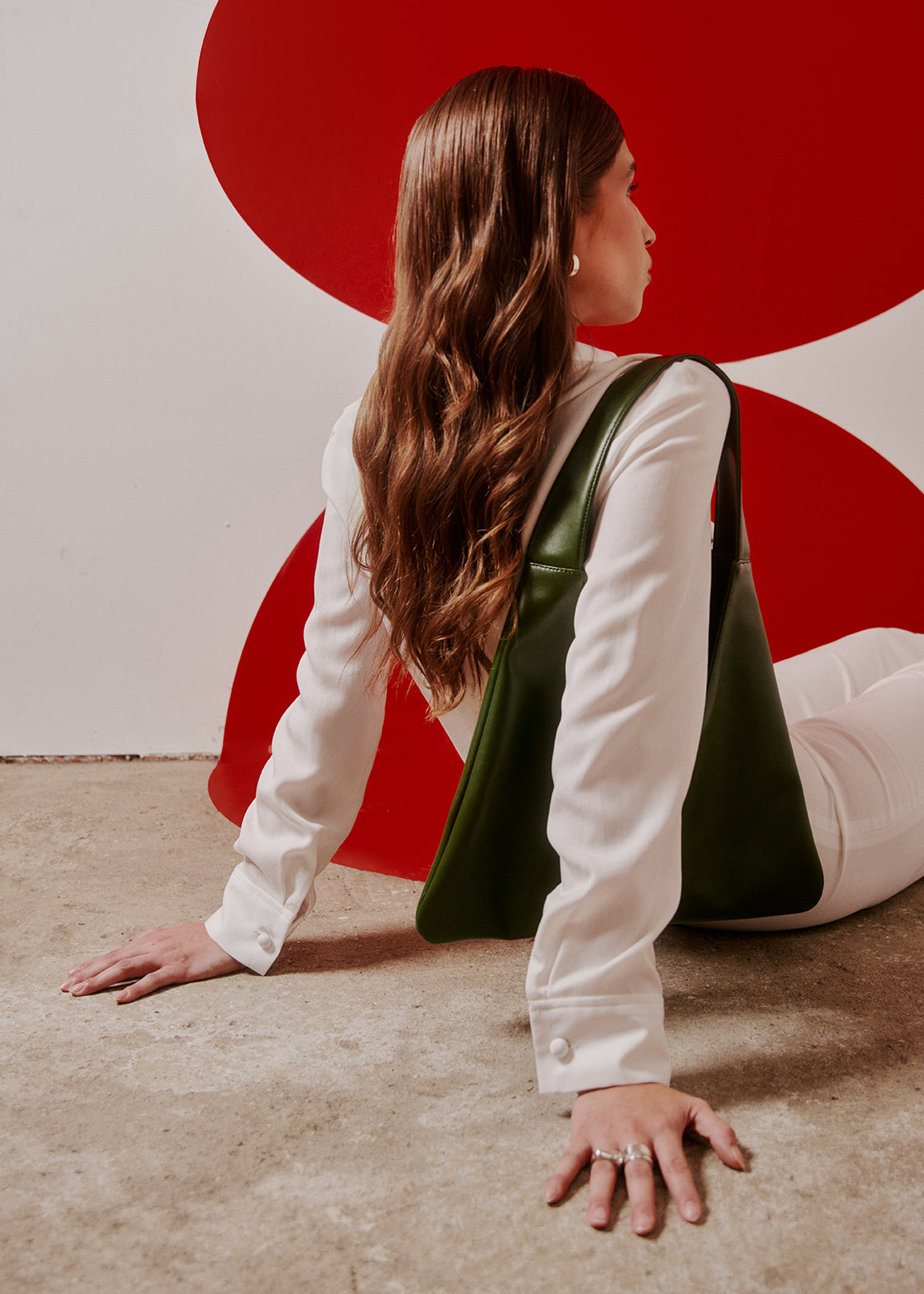 Woman sitting on the floor with a red and white abstract wall behind her carrying a green tote bag made from cactus leather