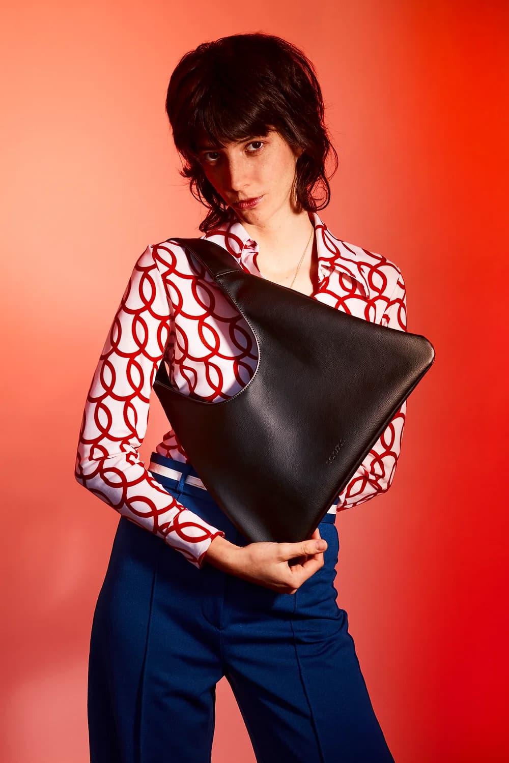 Woman holding a black sustainable handbag made from cactus leather against a red background