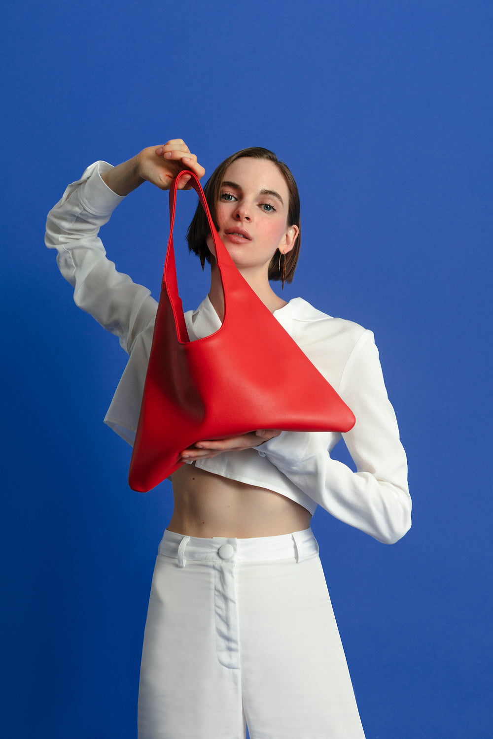 Woman holding a red handbag made from cactus leather against a blue background.