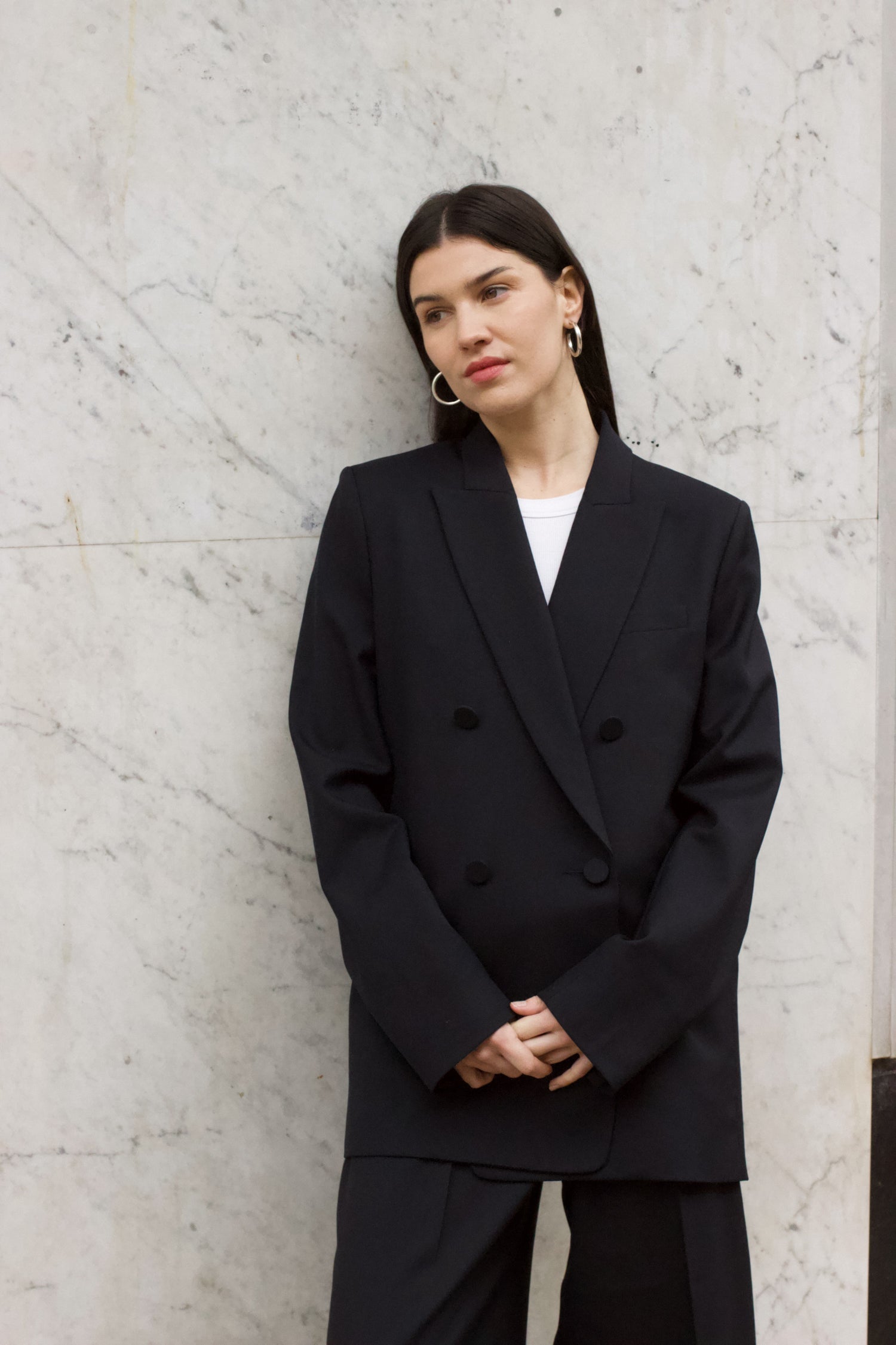 A model wearing the Christy Charcoal Wool Twill Jacket in an aesthetically background. 100% upcycled wool. 