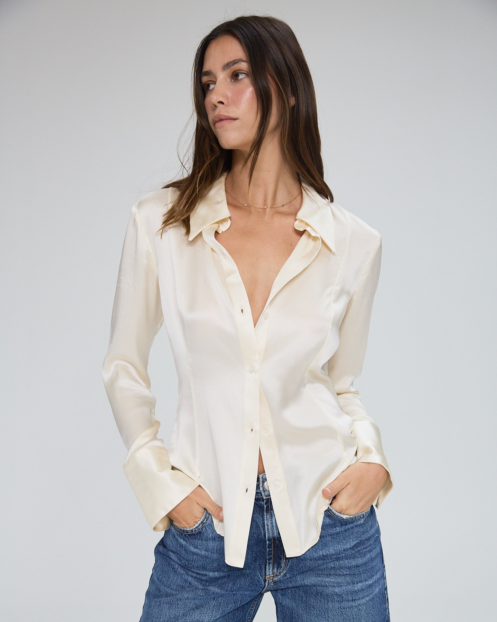 Model wearing a silk butter long sleeve button up blouse in a white background. Made from sustainable materials. 