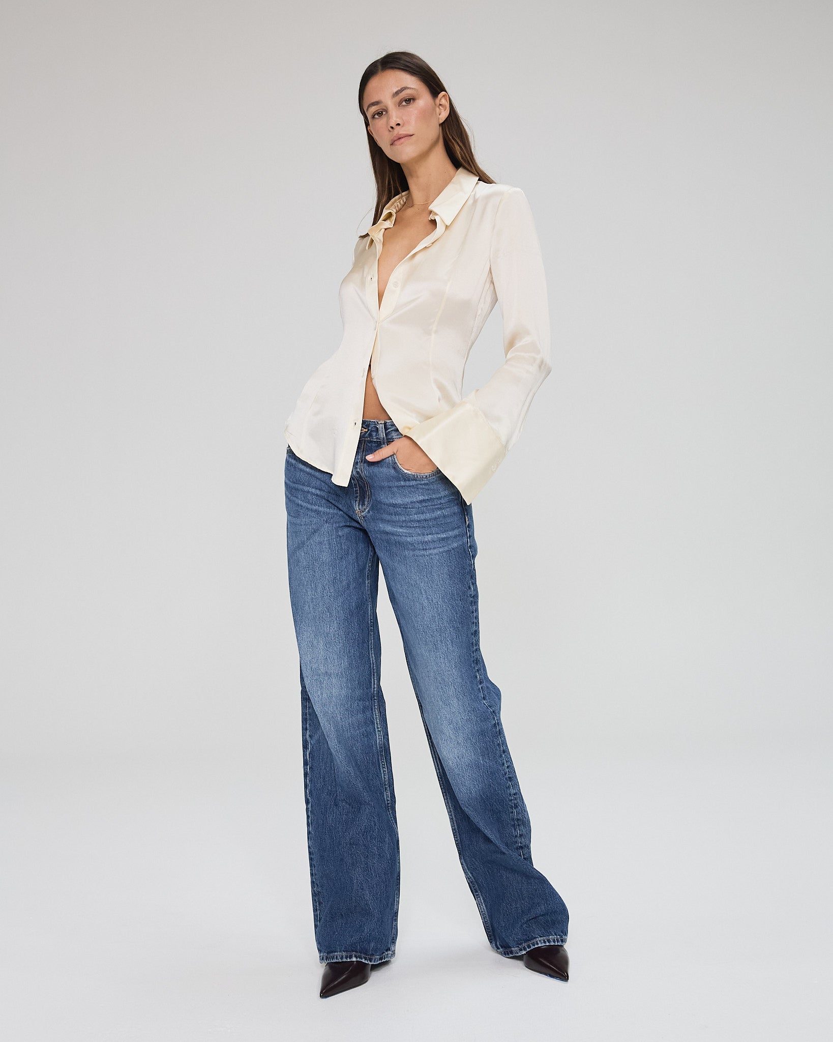 Model wearing a silk butter long sleeve button up blouse in a white background. Made from sustainable materials. 