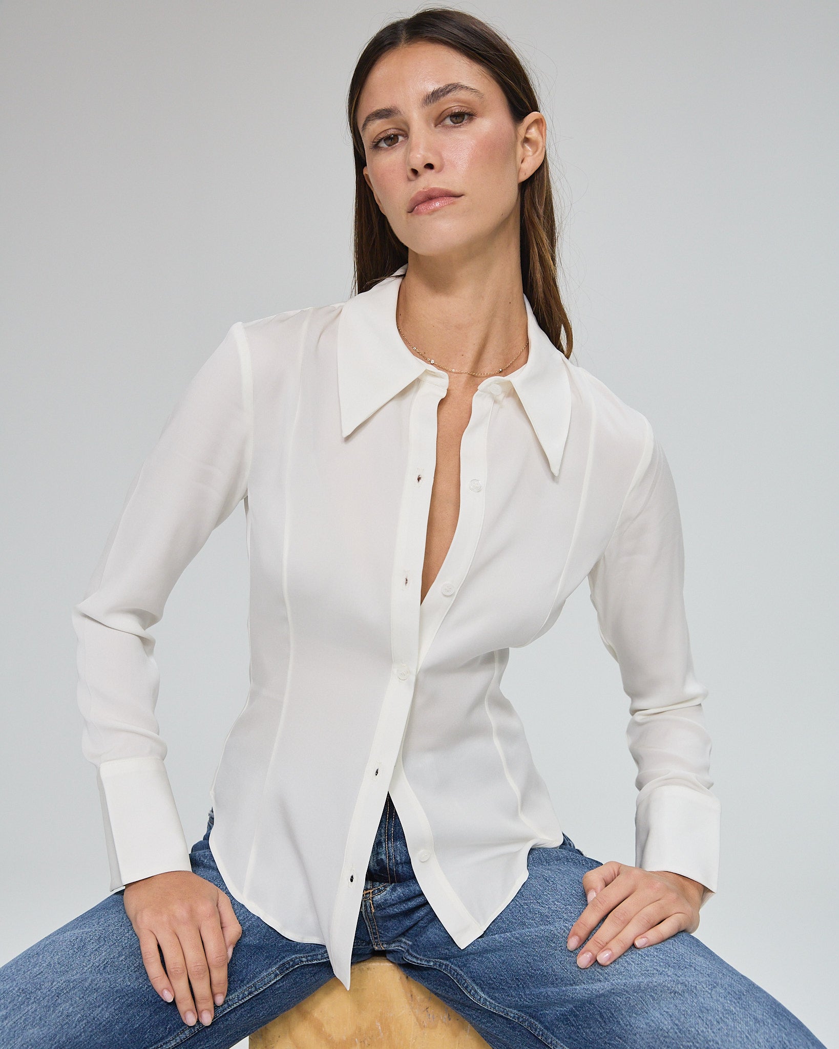 Model wearing a silk ivory long sleeve button up blouse in a white background. Made from sustainable materials.