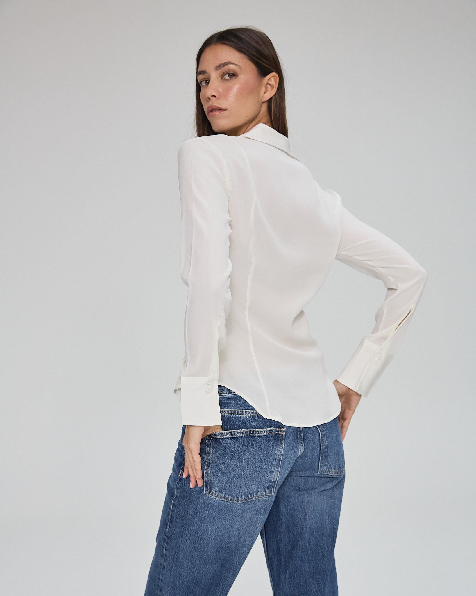 Model wearing a silk ivory long sleeve button up blouse in a white background. Made from sustainable materials.
