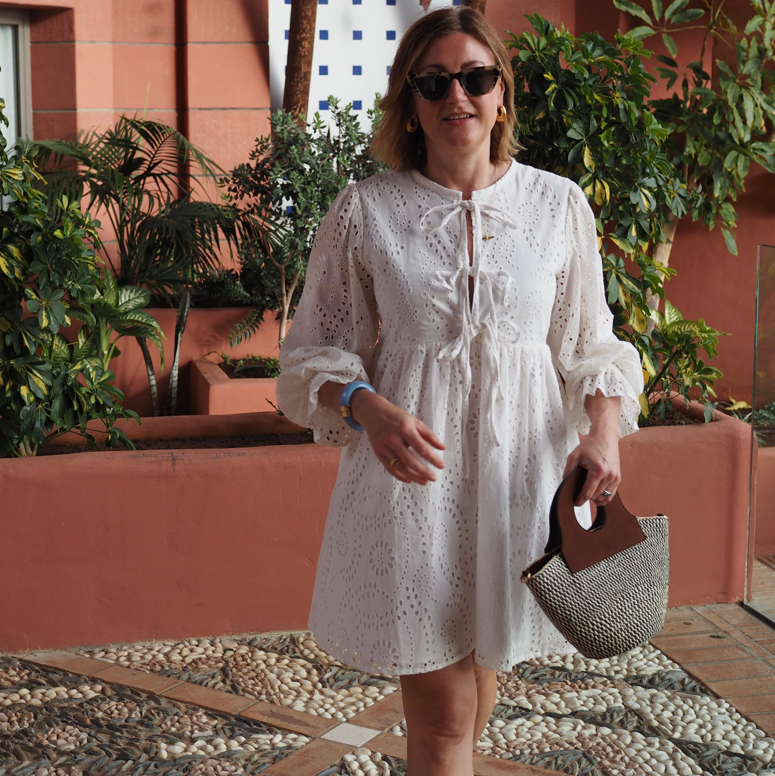 A model wearing the handheld basket bag in an aesthetically background. Handwoven sisal basket made in Kenya. Finished in England using chrome-free leather.